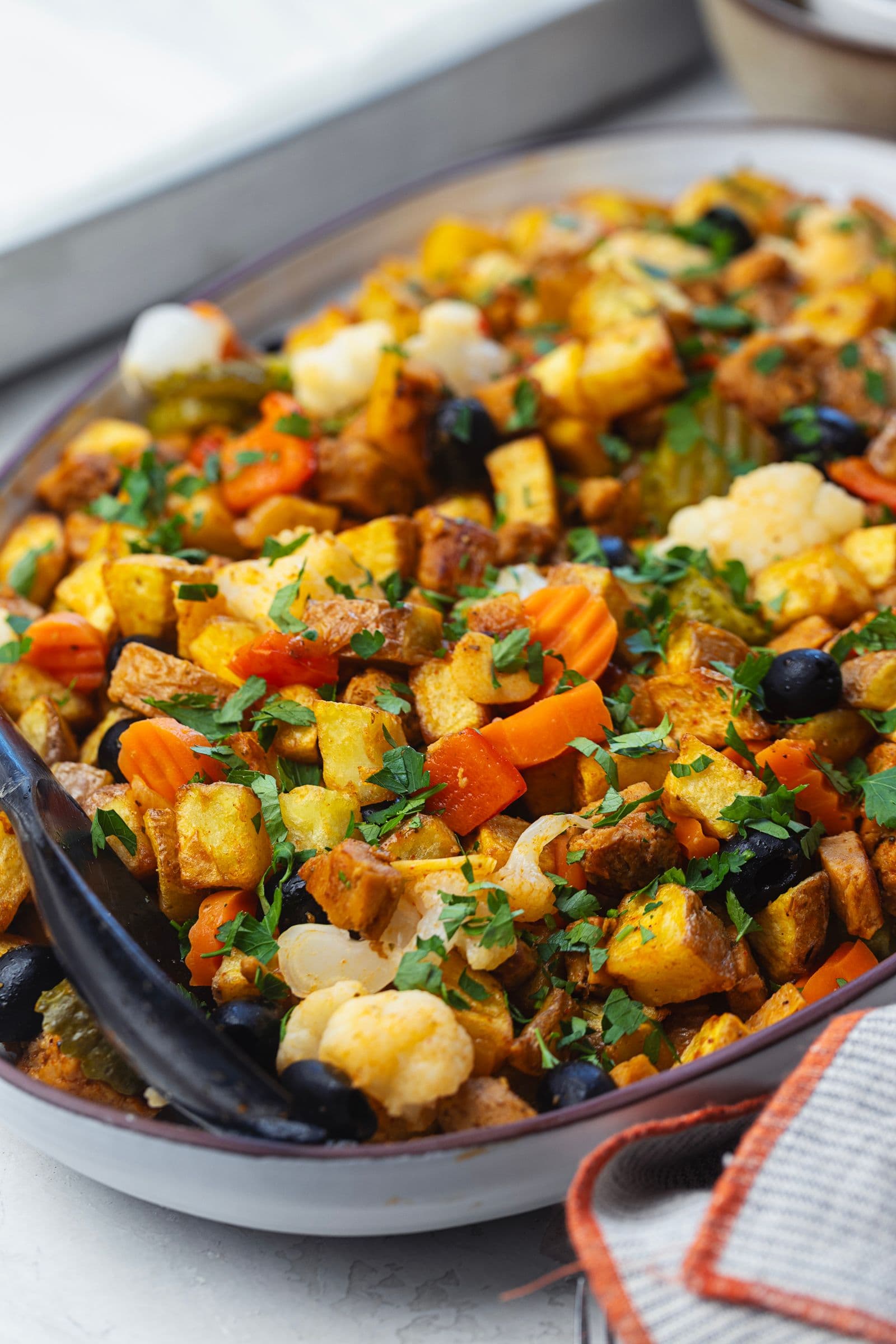 Travessa de pica pau de soja polvilhado com salsa fresca picada, com soja, batatas, pickles, azeitonas e cenoura, vista em perspectiva ligeiramente lateral