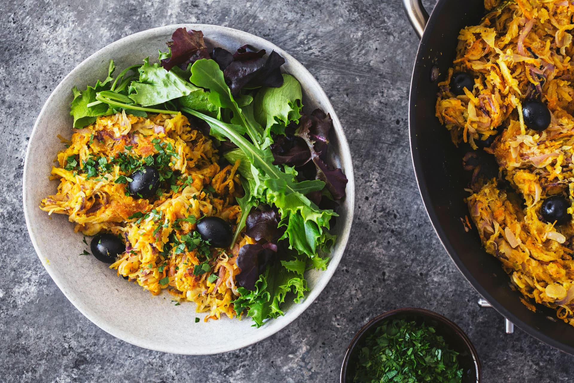 Portuguese veggie hash garnished with black olives and chopped parsley, and plated with fresh green salad on the side.