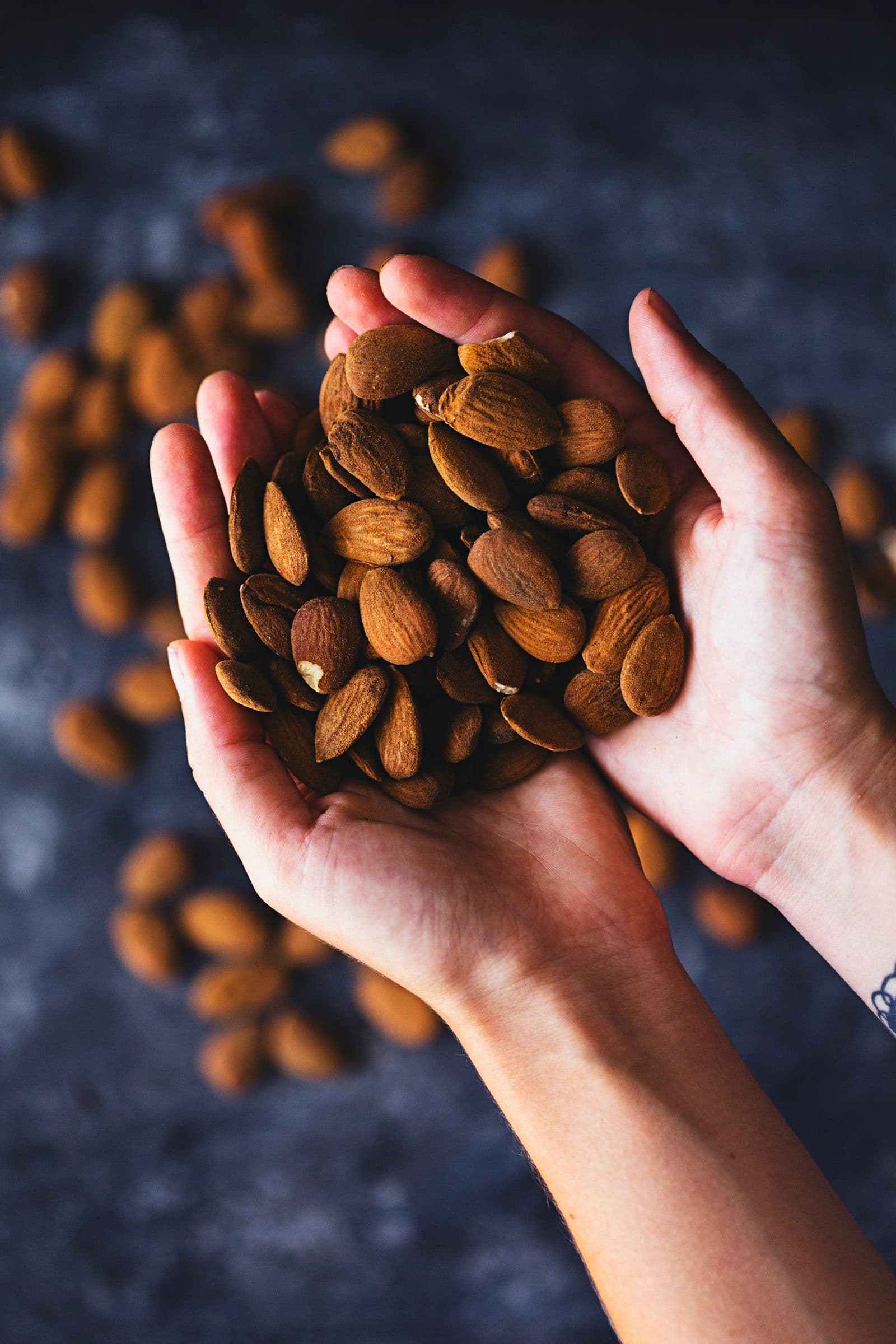 A pair of hands holding raw almonds over a dark background.