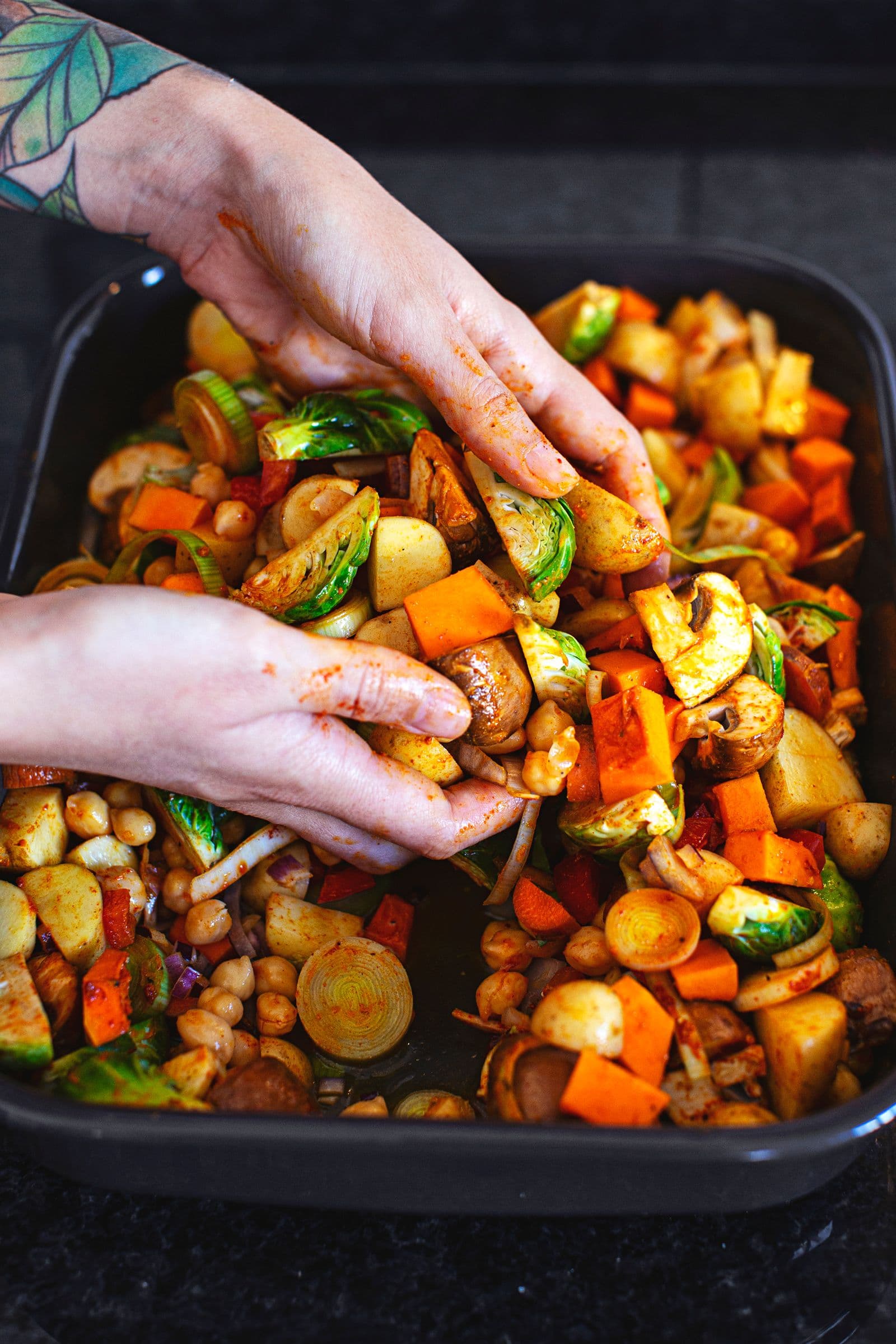 Hands mixing raw vegetables and chickpeas with spices for a savoury crumble.