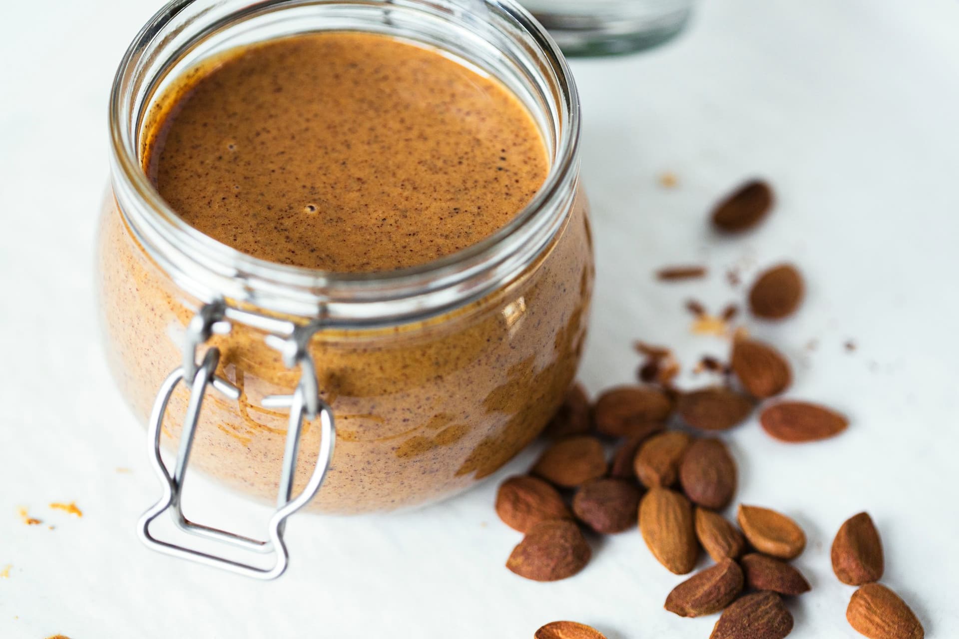 Jar of homemade almond butter surrounded by roasted almonds.