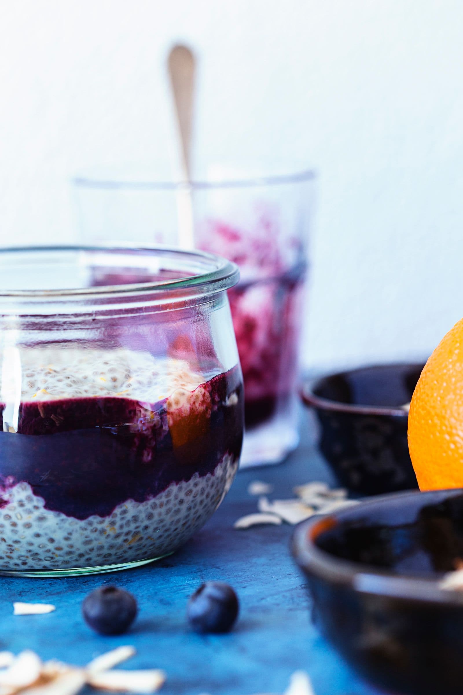 Layered chia pudding in a glass with dark blueberry purée and orange on the side.