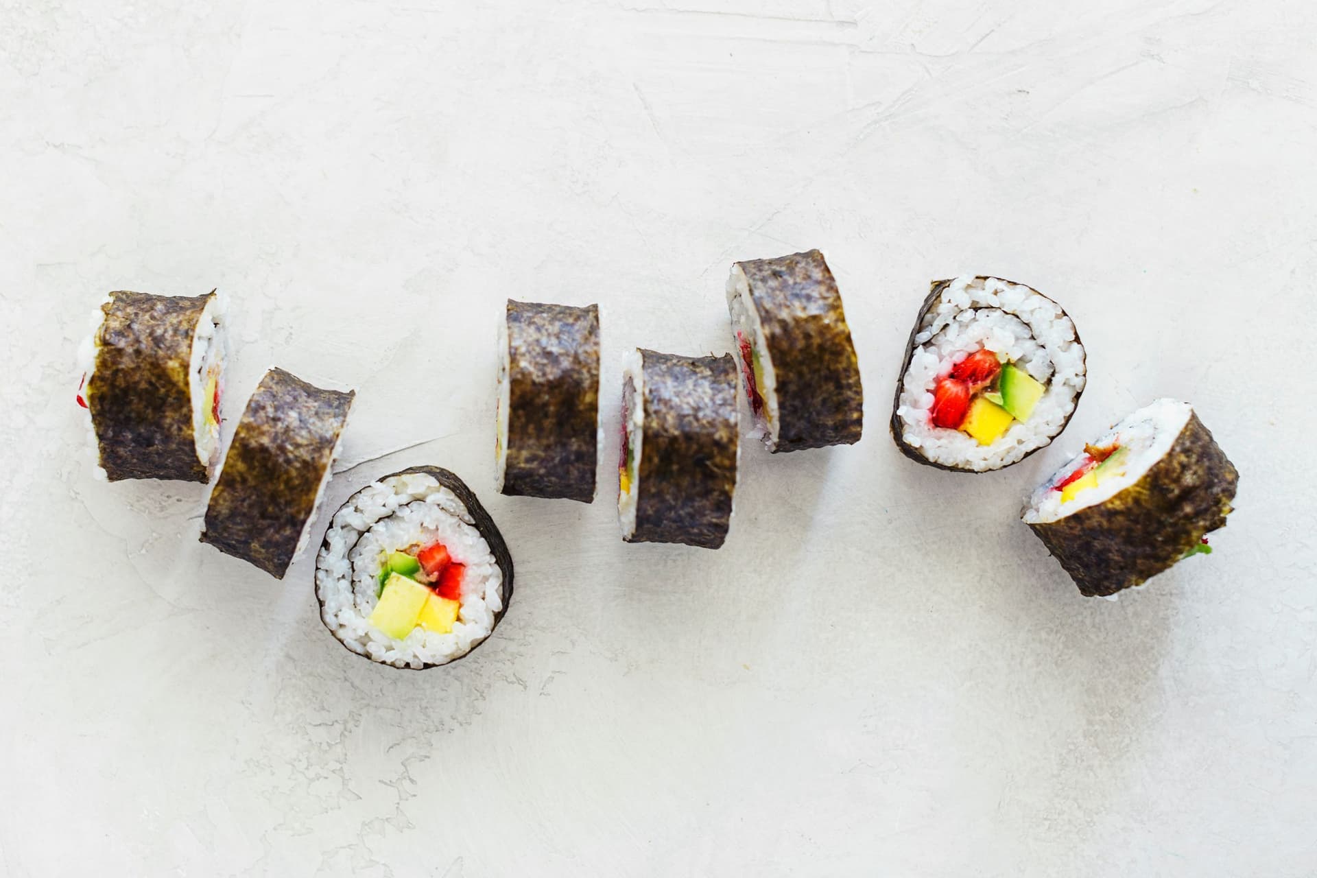 Rolinhos de sushi vegan cortados e alinhados numa superfície branca.