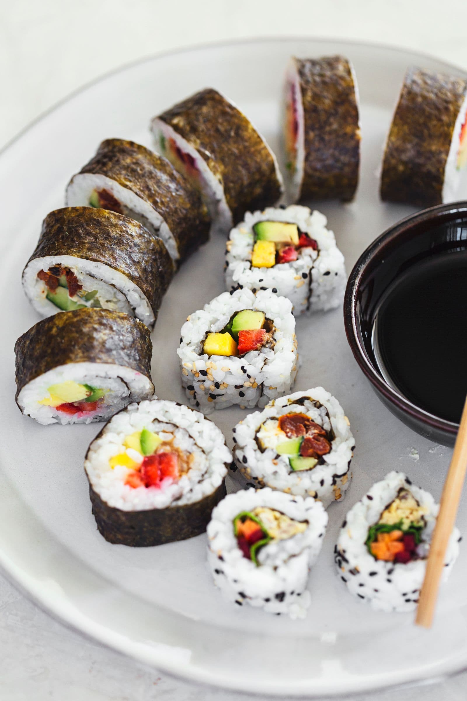 Plate of assorted vegan sushi rolls served with soy sauce for dipping.