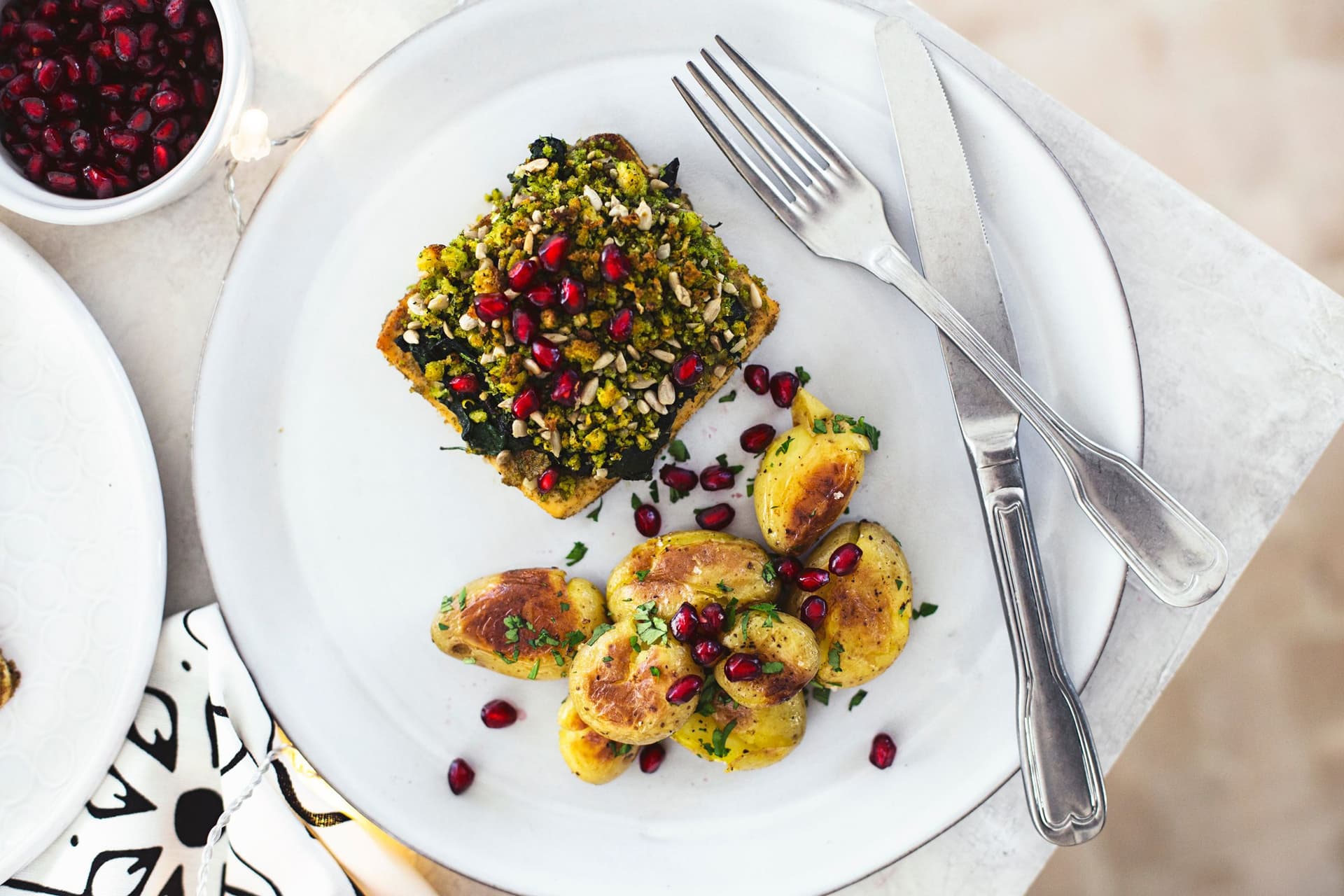 A square of tofu roast and a few roasted potatoes on a white plate with a fork.