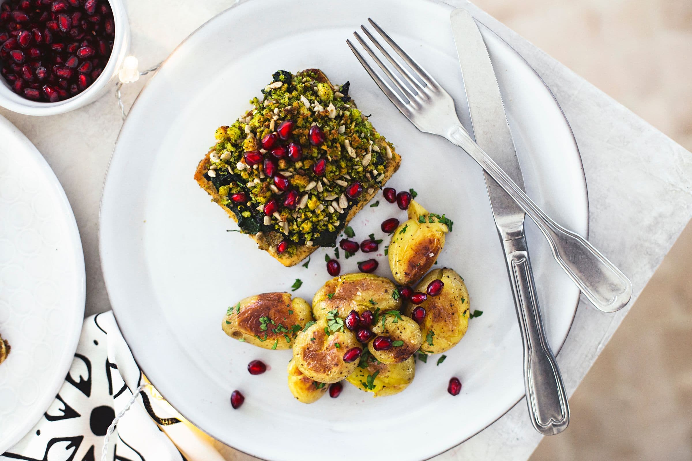 Quadrado de tofu assado com batatinhas num prato branco acompanhado de um garfo.