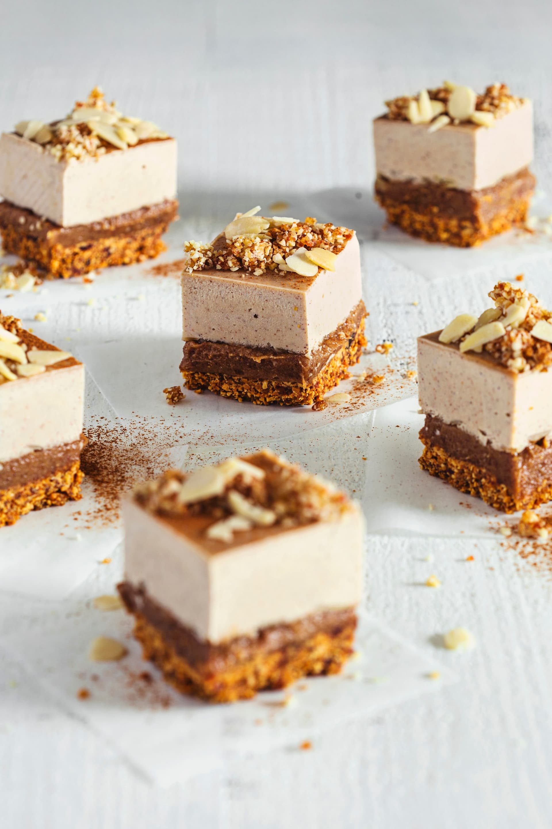 Fatias de cheesecake vegan de amêndoa e caramelo salgado sobre superfície branca, com frutos secos picados por cima.