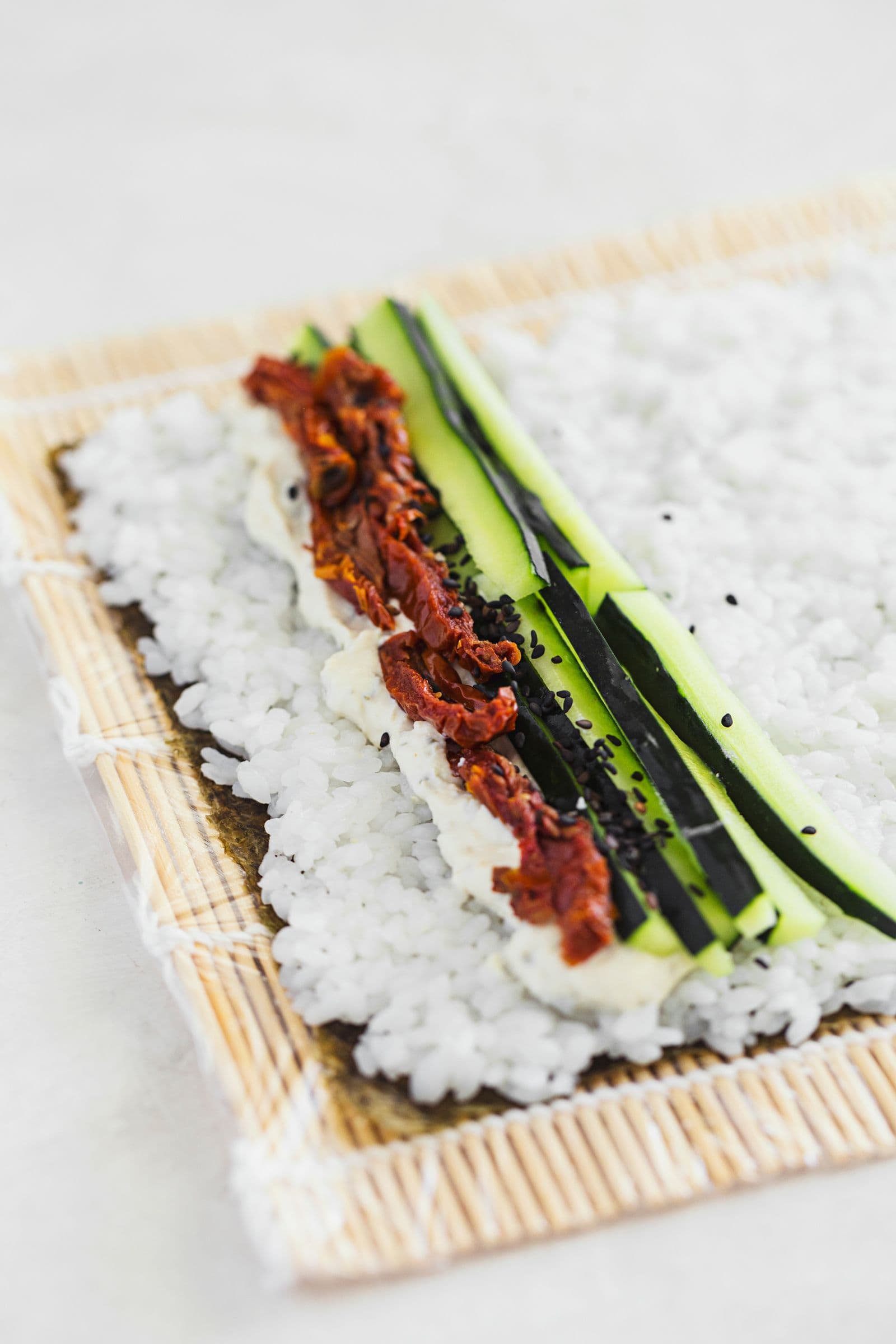 Open sushi roll topped with veggie strips and spread before rolling.