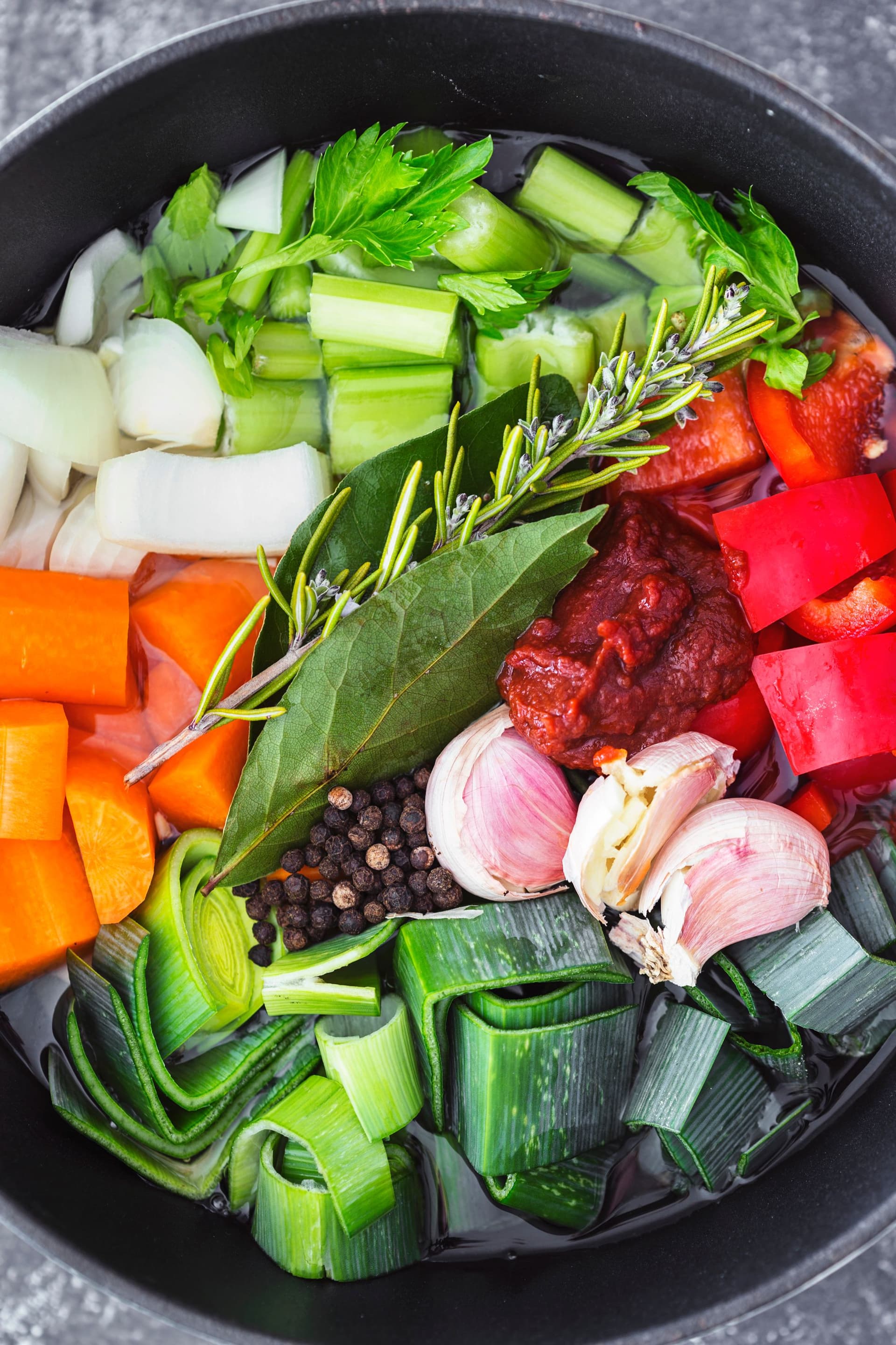 Vegetais frescos, ervas aromáticas, alho e pimenta em grão prontos para preparar caldo de legumes caseiro.
