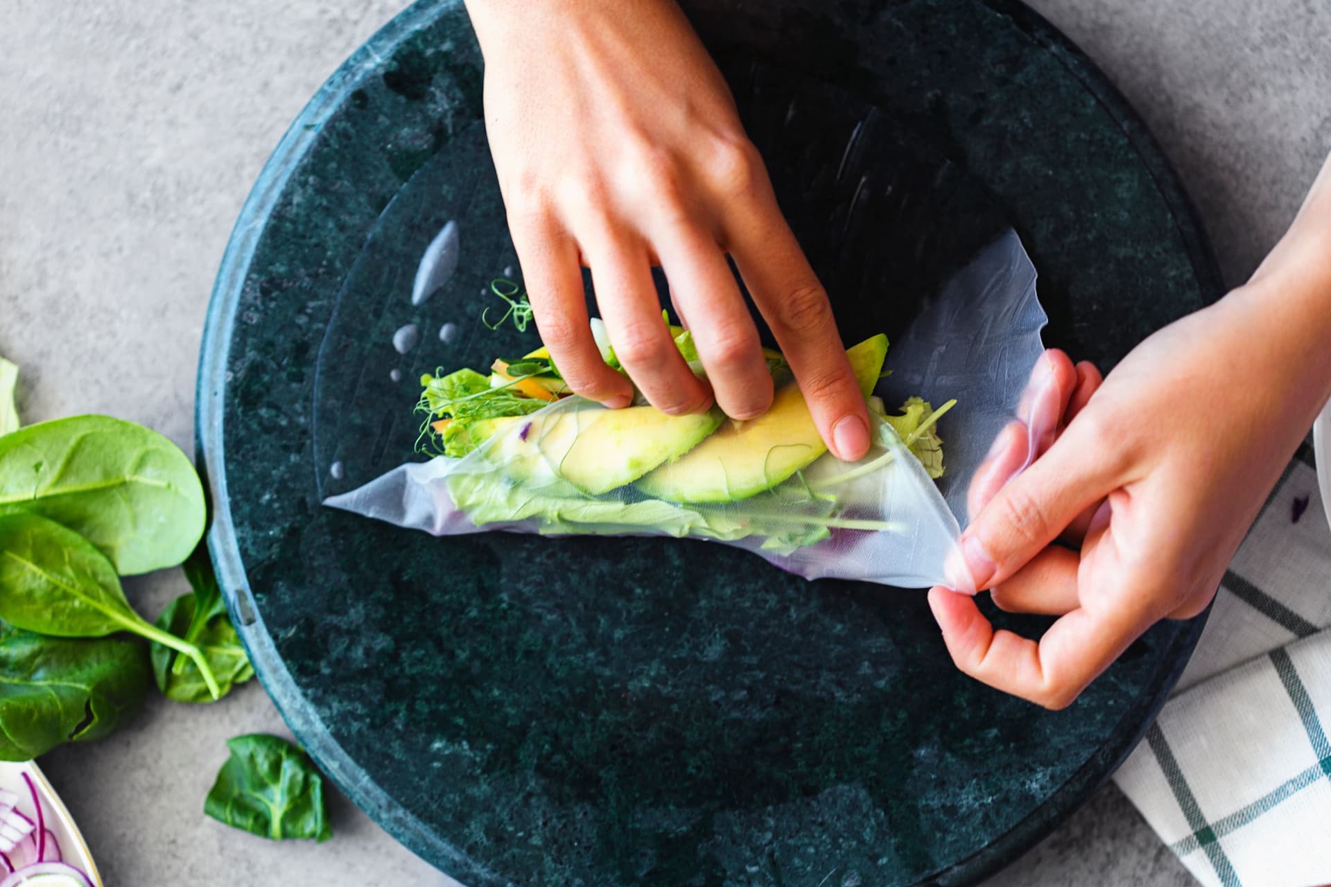 Hands folding the rice paper wrap over vibrant vegetables.