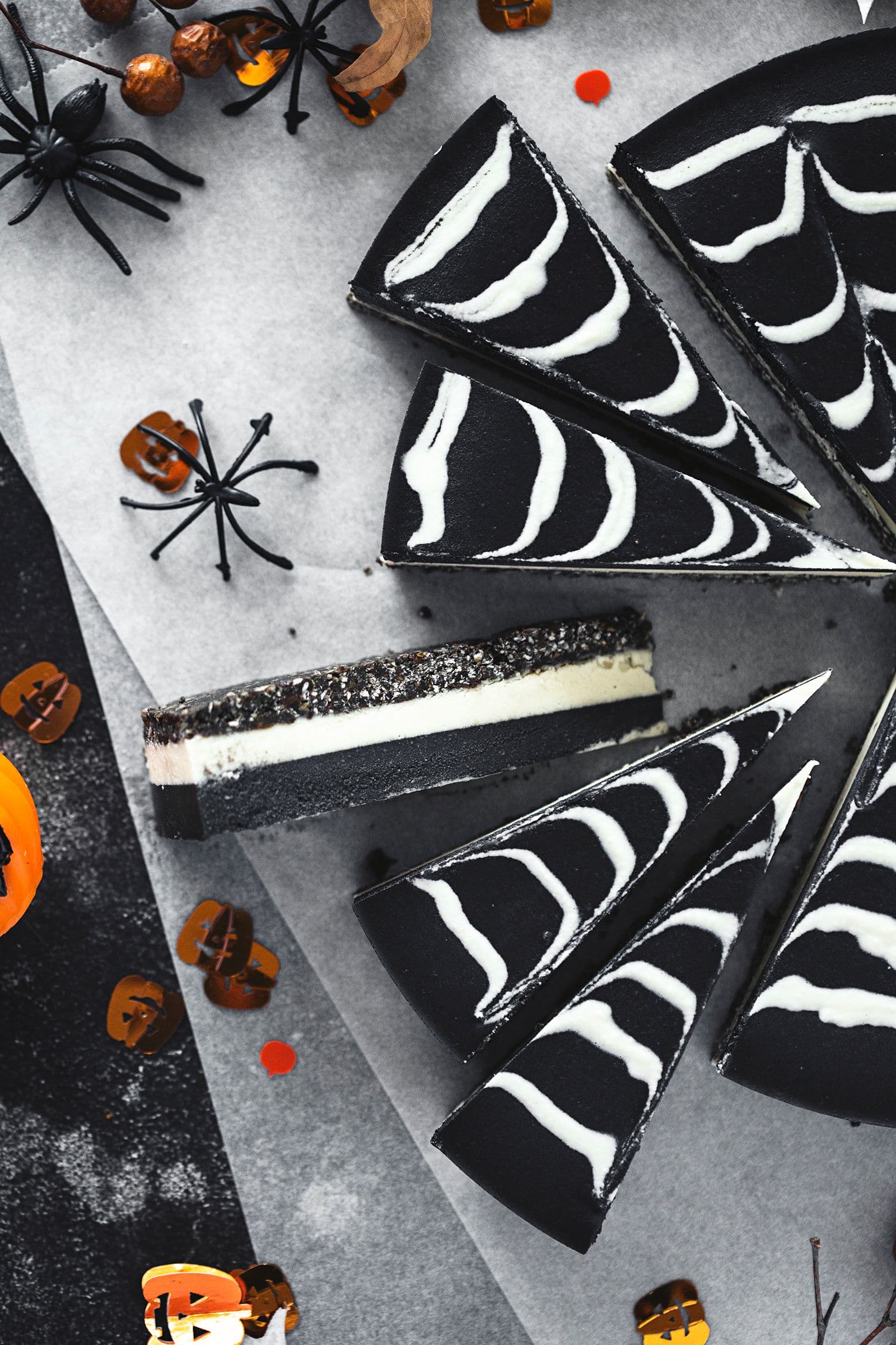 Fatias de cheesecake de Halloween rodeadas de mini abóboras e aranhas de brincar.