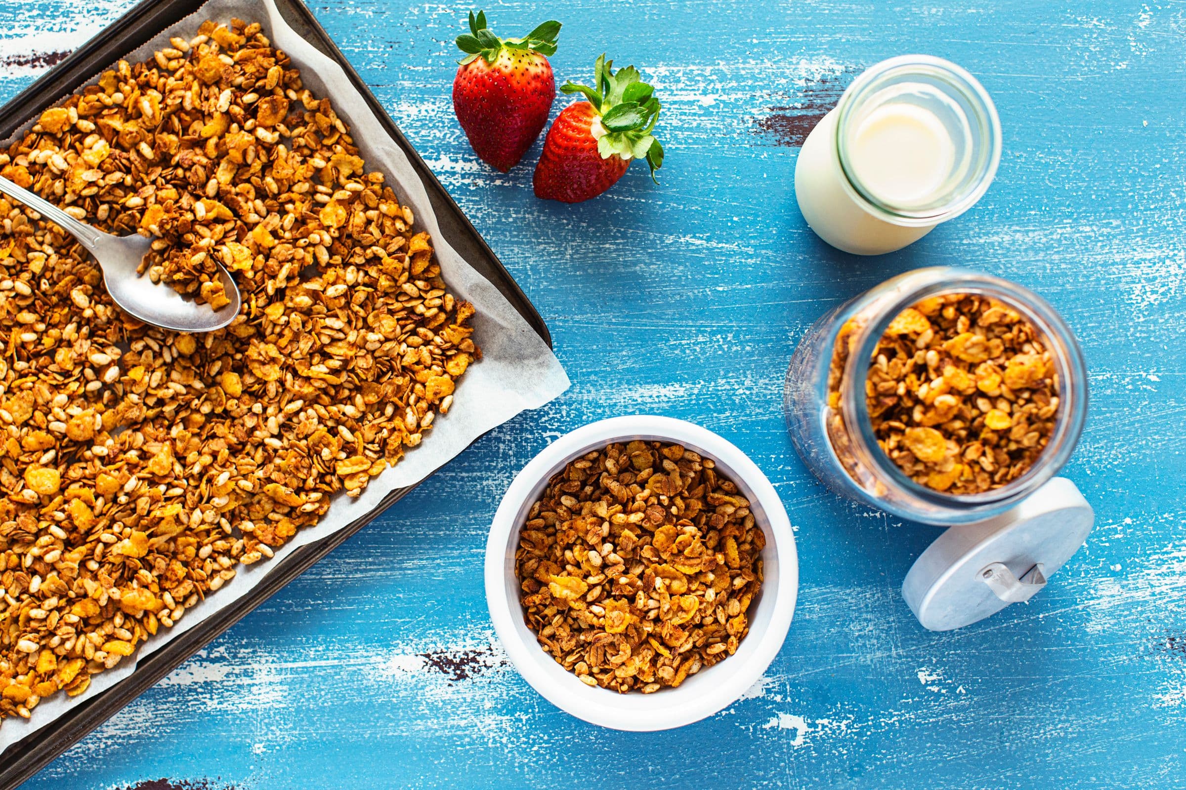 Baked cornflake granola being spooned into glass jars for storage.