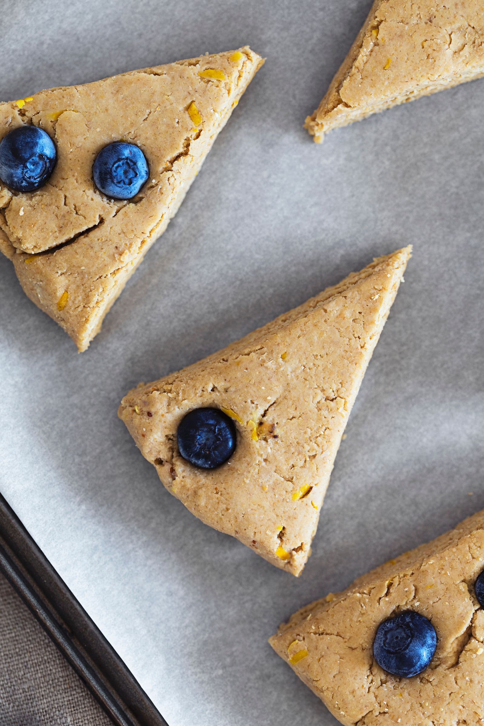 Close-up of scone dough pieces dotted with juicy blueberries on a baking sheet.