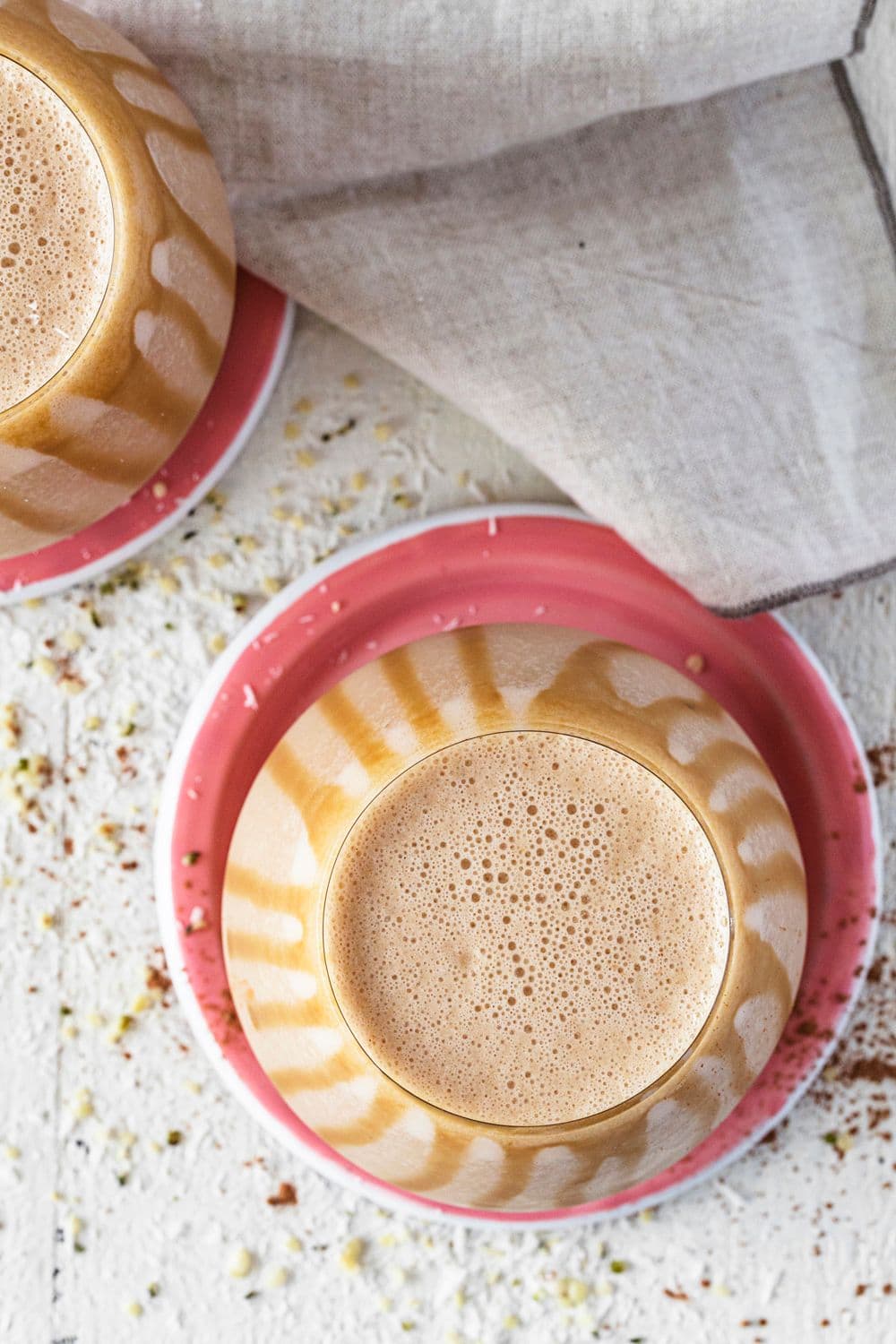 Rounded glass with salted caramel and peanut butter smoothie, drizzled with caramel sauce, on a pink coaster.