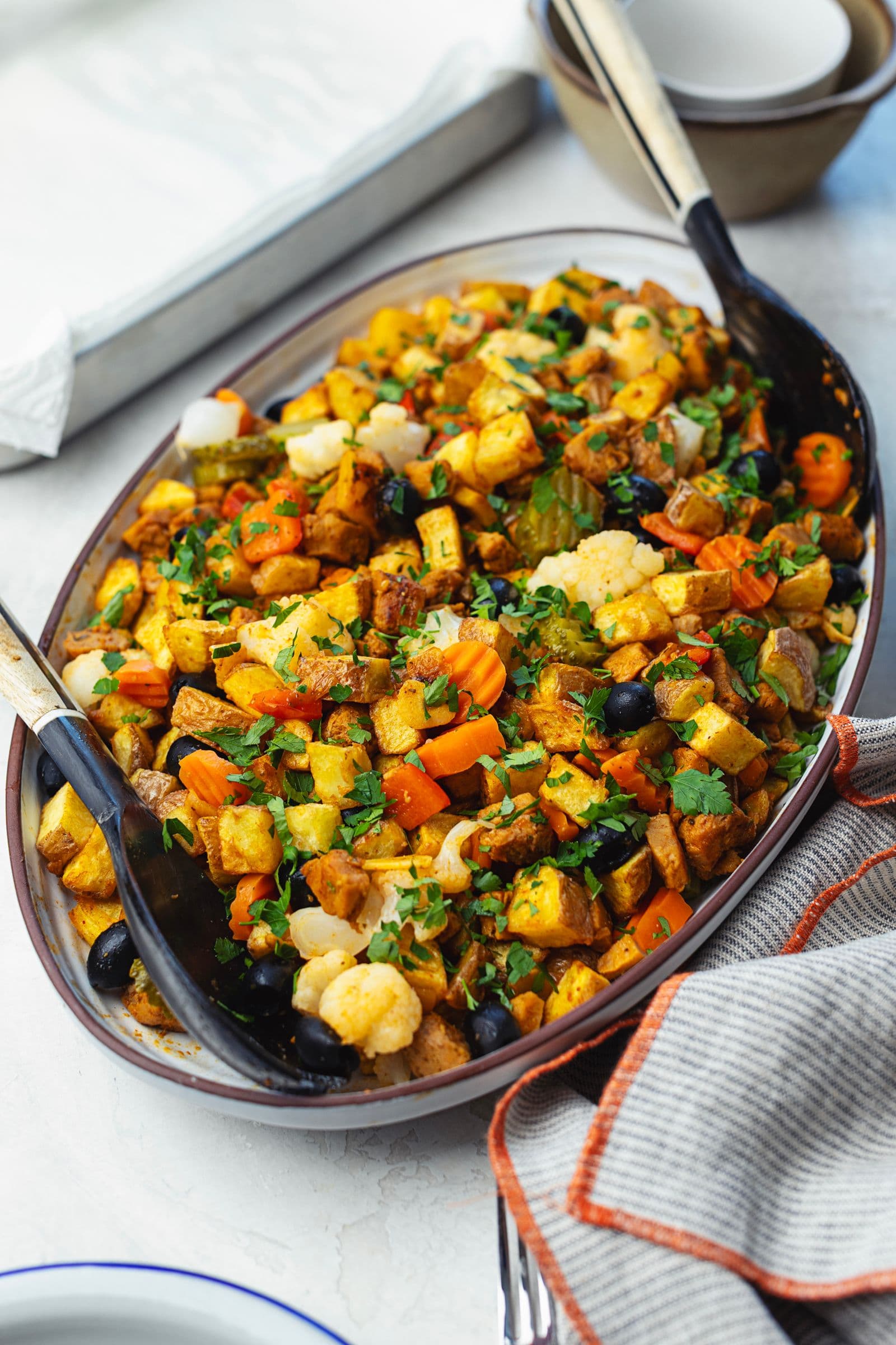 Travessa oval de pica pau de soja com batatas fritas, azeitonas pretas, pickles, cenoura e couve-flor, polvilhada com salsa fresca e fotografada em ângulo lateral