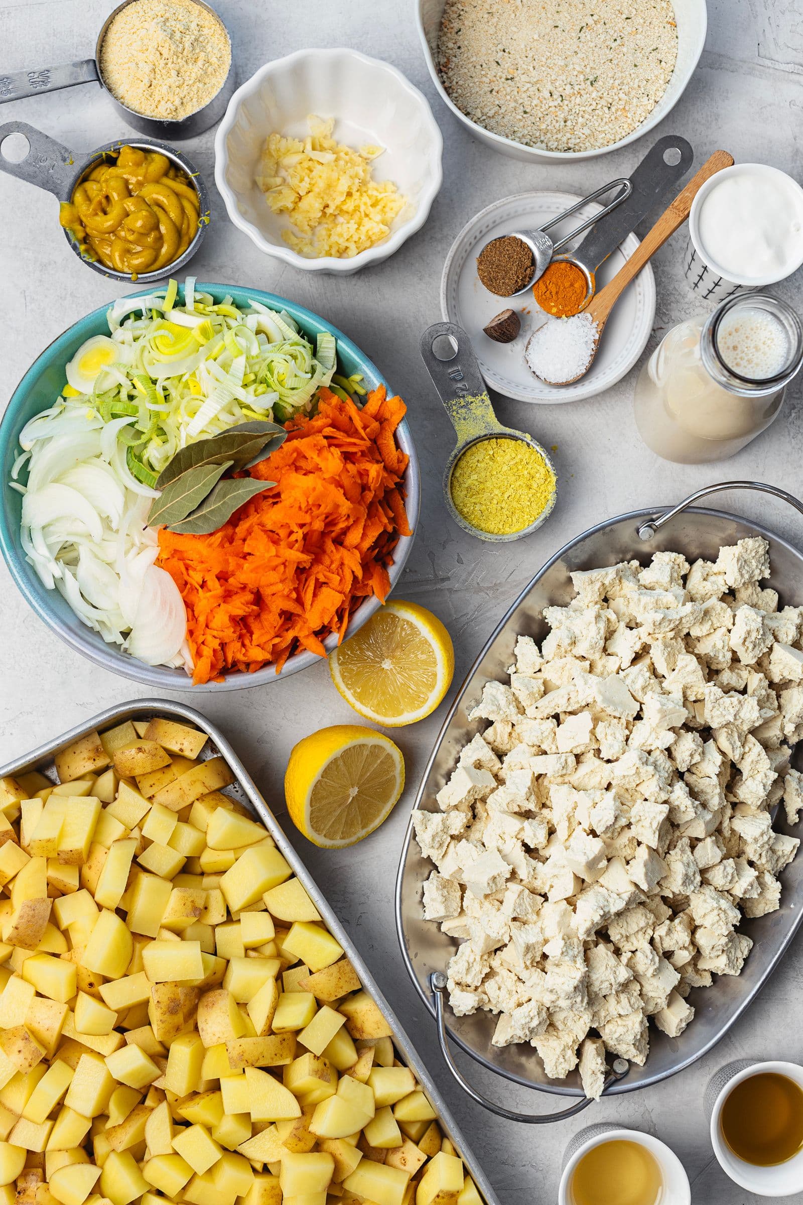 Ingredientes preparados para o gratinado: tofu em pedaços, batatas, legumes fatiados e ingredientes do béchamel colocados em tigelas.