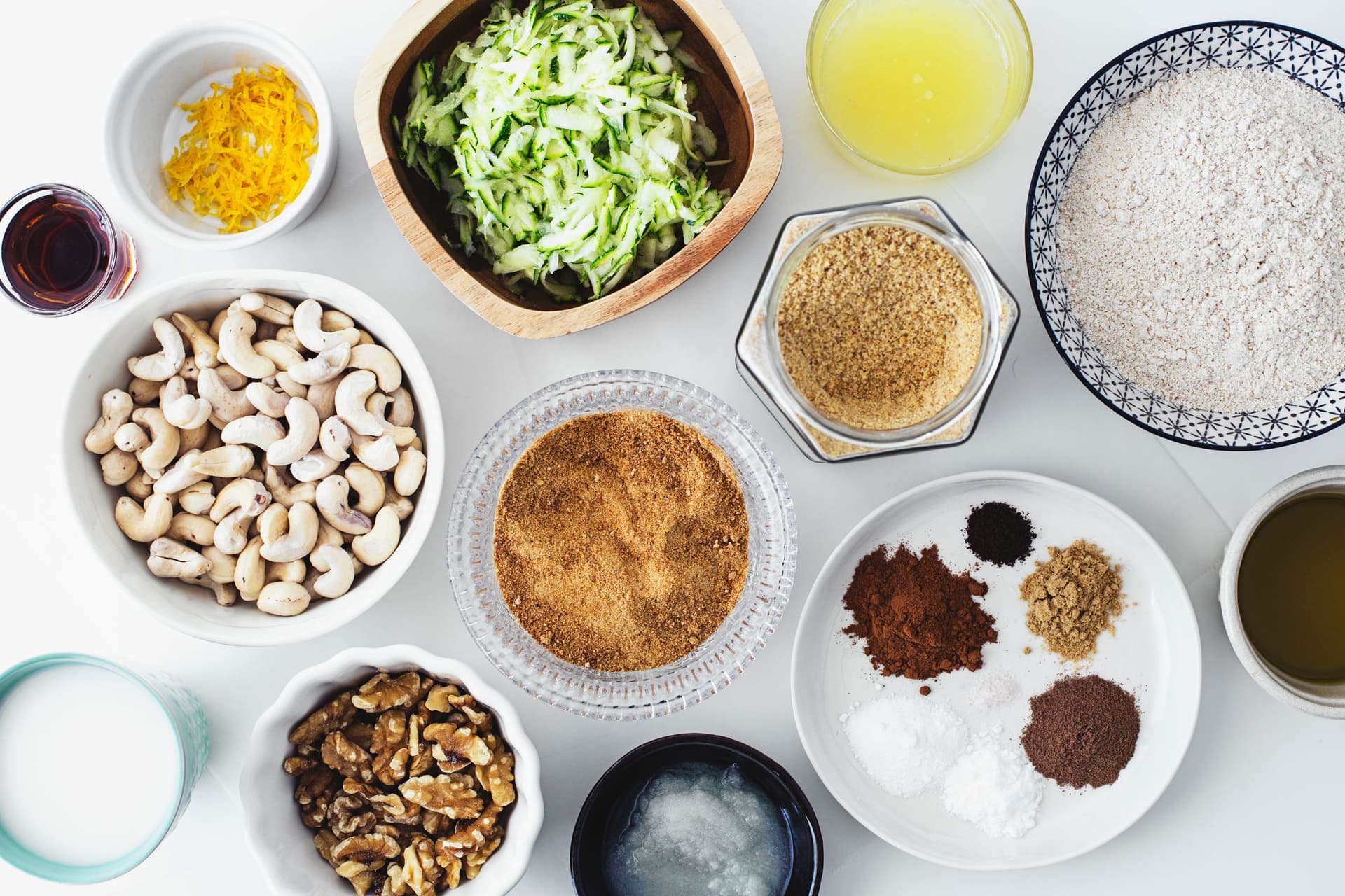 Todos os ingredientes secos e húmidos para o bolo de curgete e limão dispostos em taças pequenas.