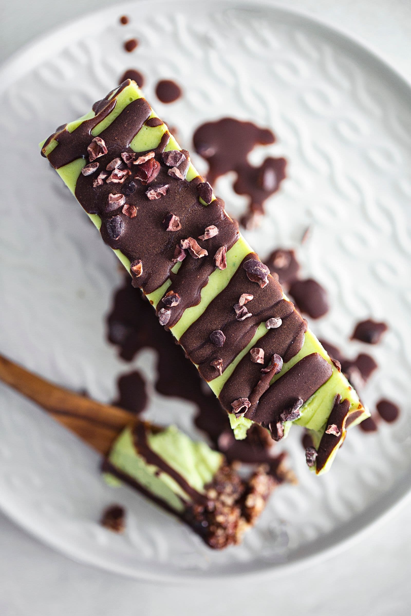 Close-up de fatia de cheesecake vegan de menta e chocolate com base de frutos secos, coberta com chocolate derretido e nibs de cacau.