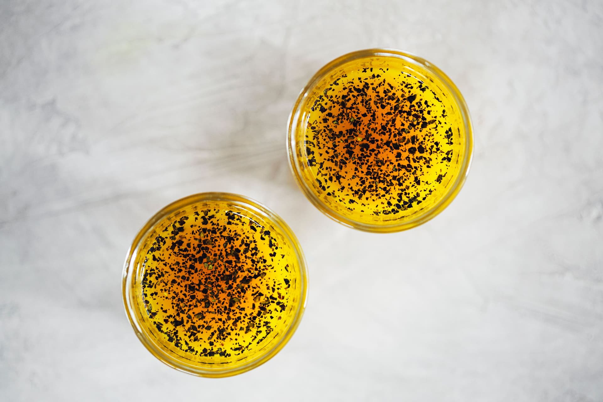 Overhead shot of two small glasses of golden syrup sprinkled with black pepper.