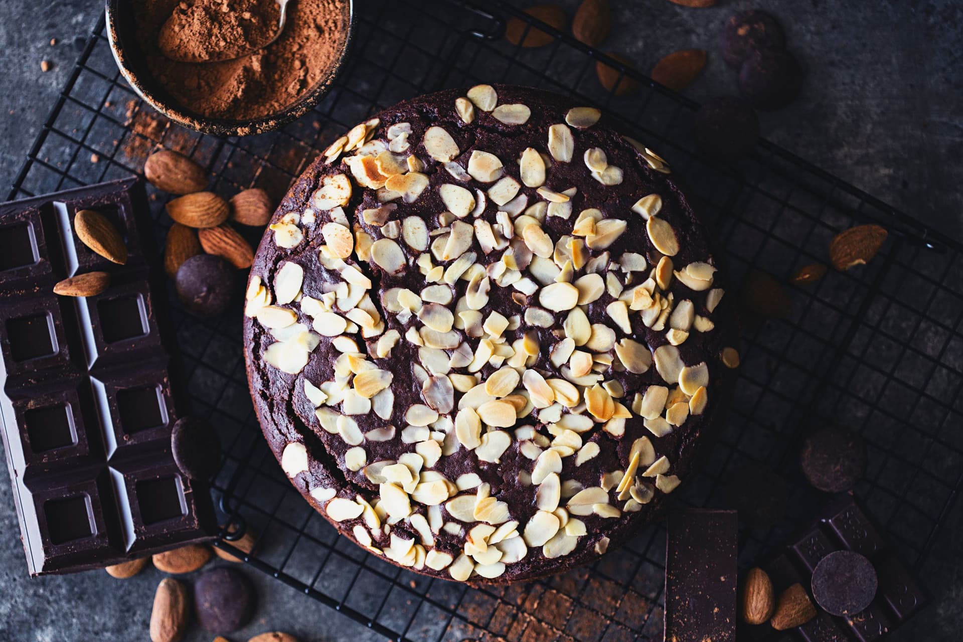Bolo de chocolate com amêndoas inteiro sobre uma grelha, rodeado de chocolate e amêndoas.