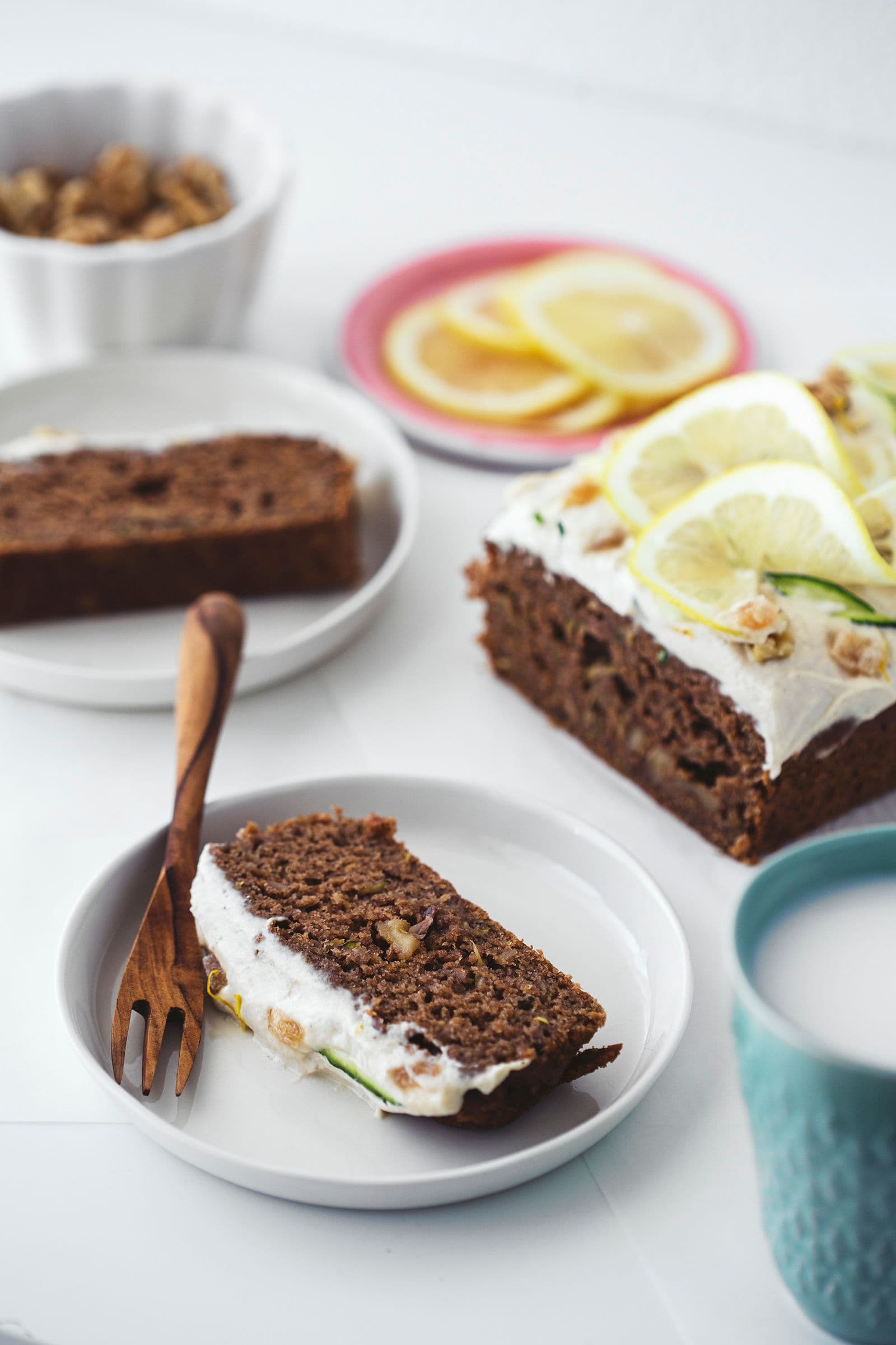 Duas fatias de bolo de curgete e limão servidas com cobertura e decoração de limão.