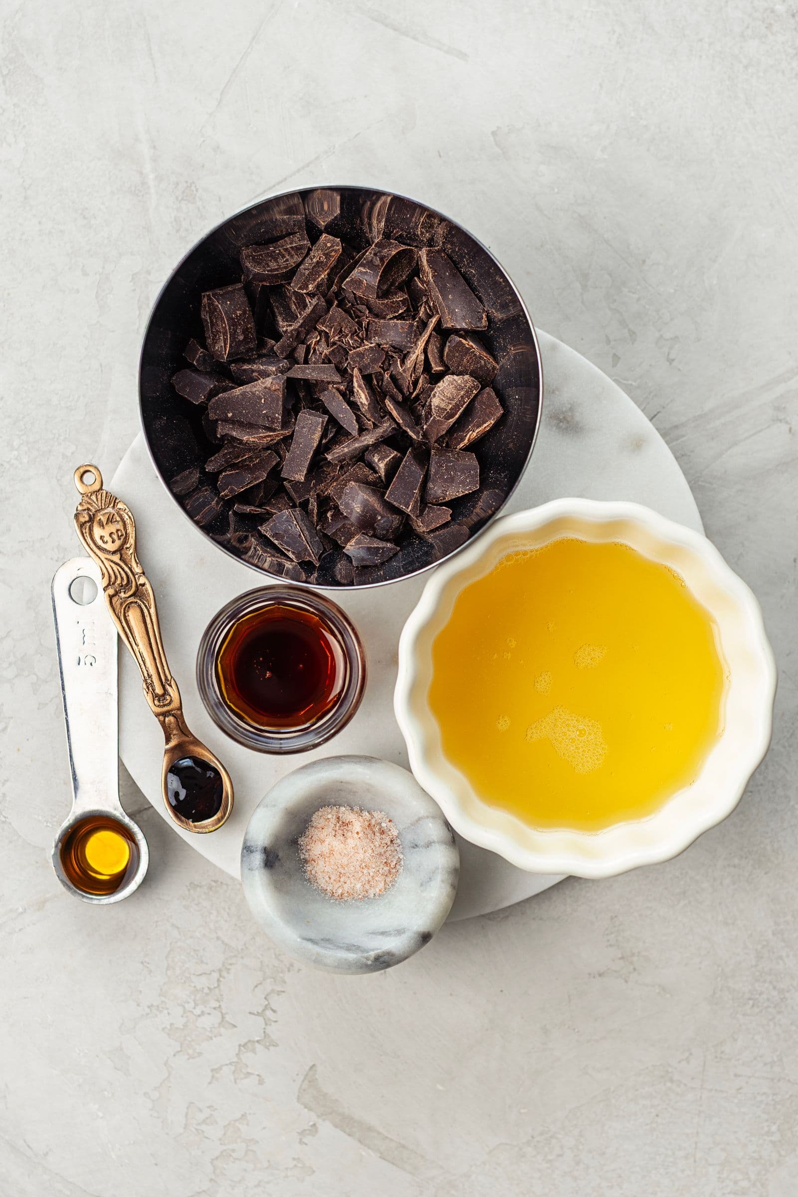 Ingredientes para mousse de chocolate vegan dispostos sobre uma superfície clara, incluindo chocolate negro picado, aquafaba, xarope de ácer, baunilha e sal.