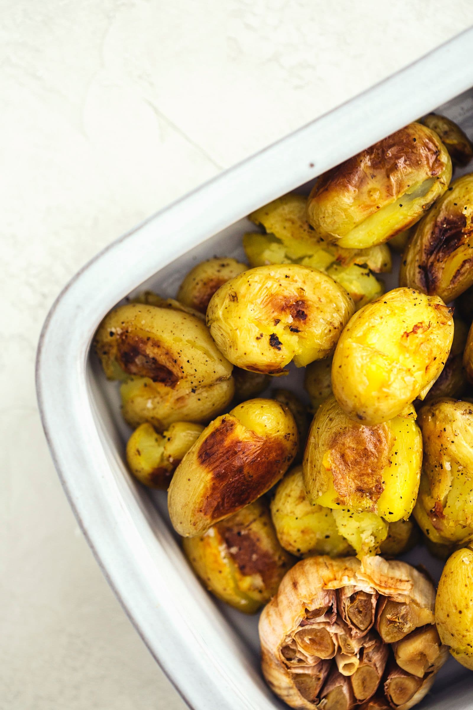 Golden roasted baby potatoes with garlic cloves in a white baking dish.