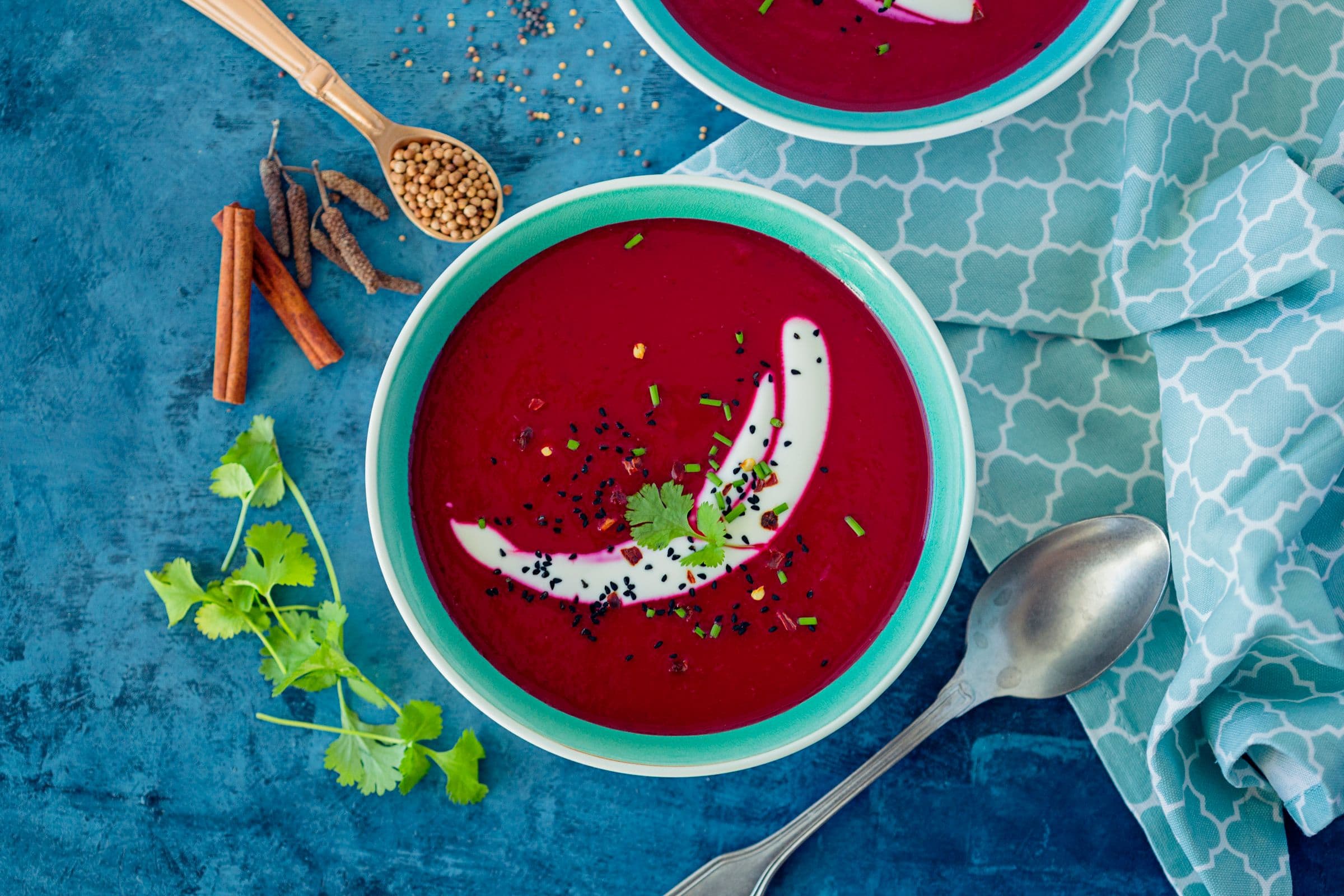 Sopa vibrante de beterraba e maçã reineta servida numa taça turquesa, com iogurte e ervas frescas, sobre fundo azul.