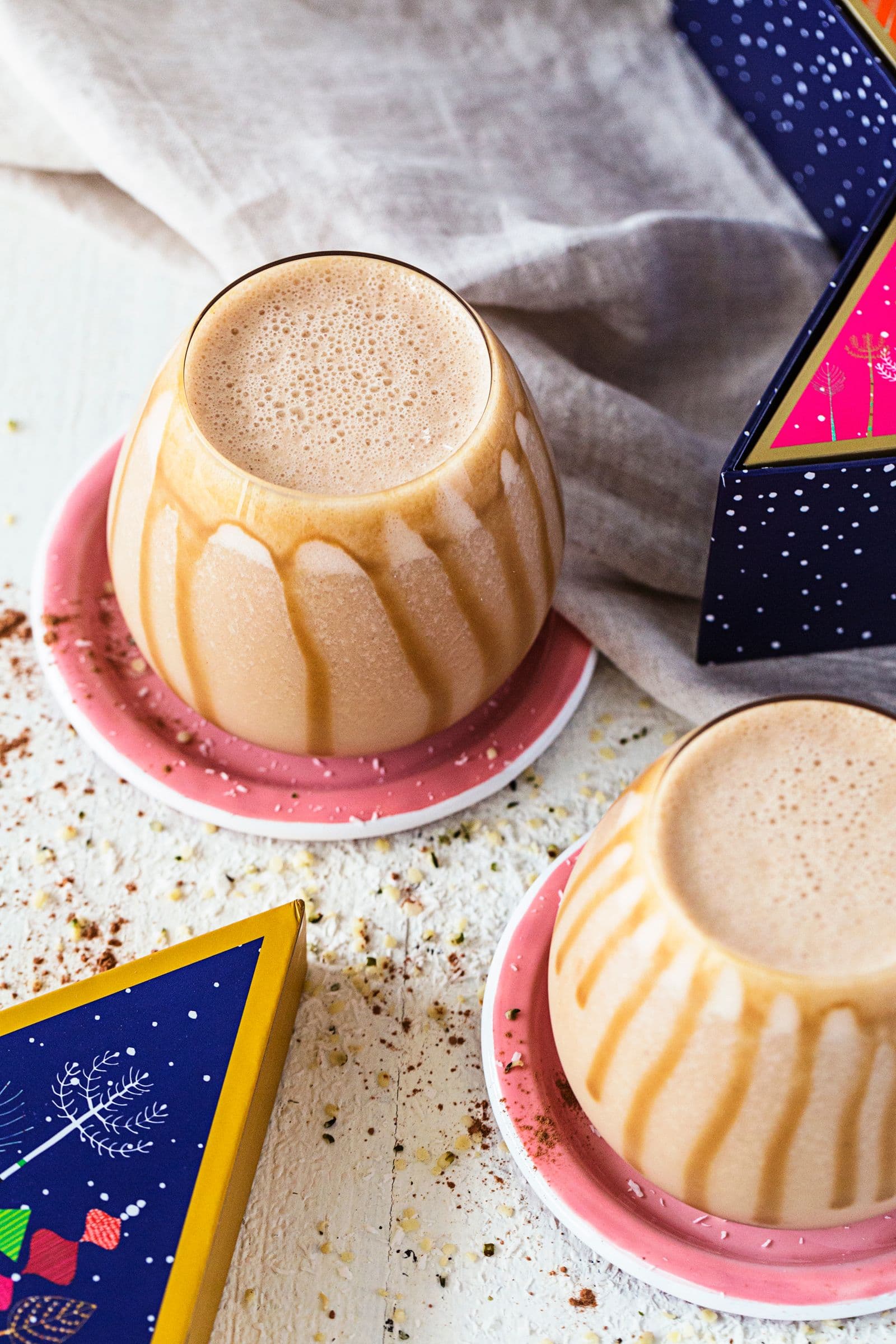 Copos arredondados com smoothie de caramelo salgado e manteiga de amendoim, servidos em bases cor-de-rosa, com fio de caramelo escorrido pelas laterais.