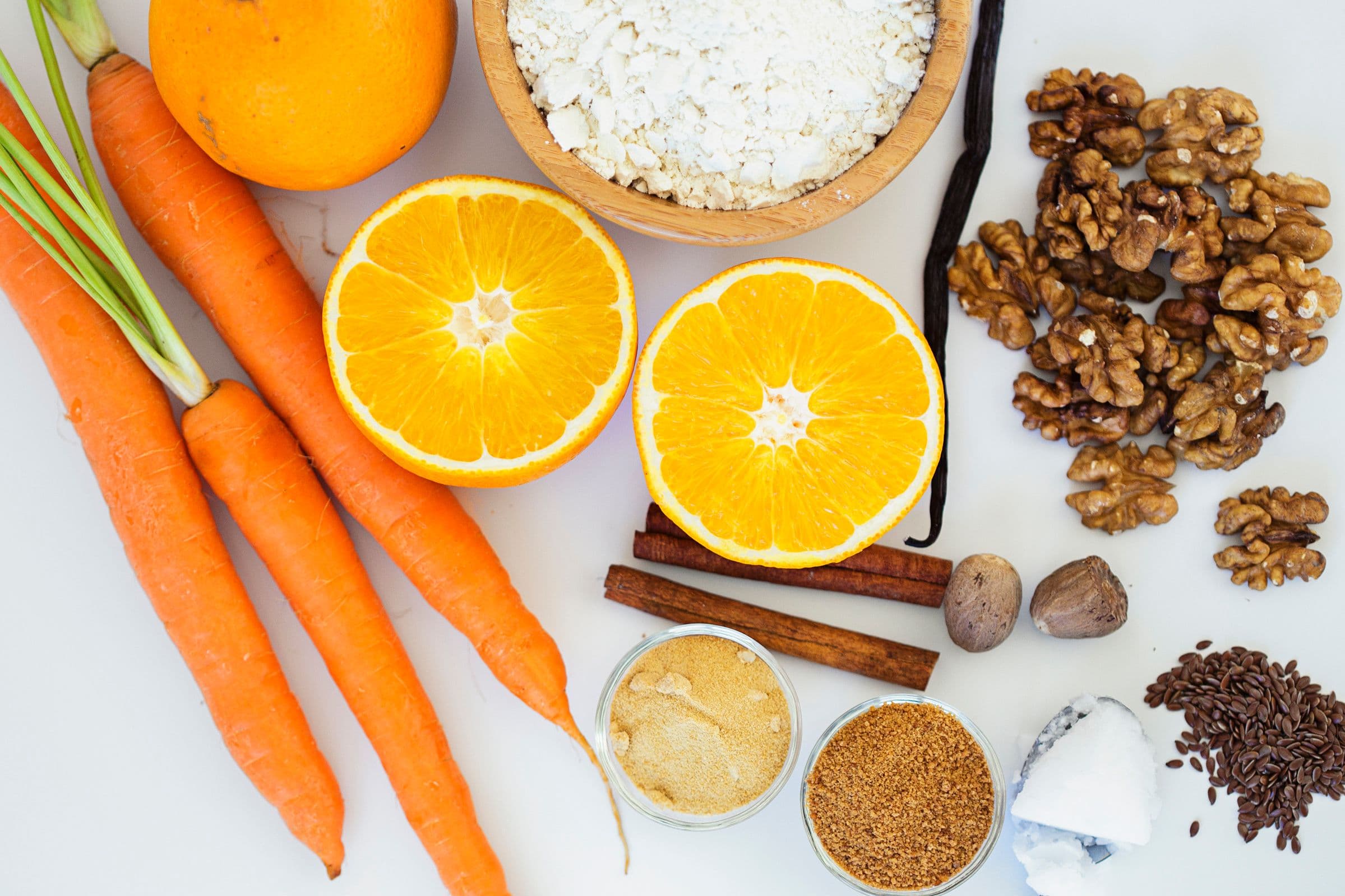 Flat lay of ingredients including carrots, orange, walnuts, flour, spices, and sugar.