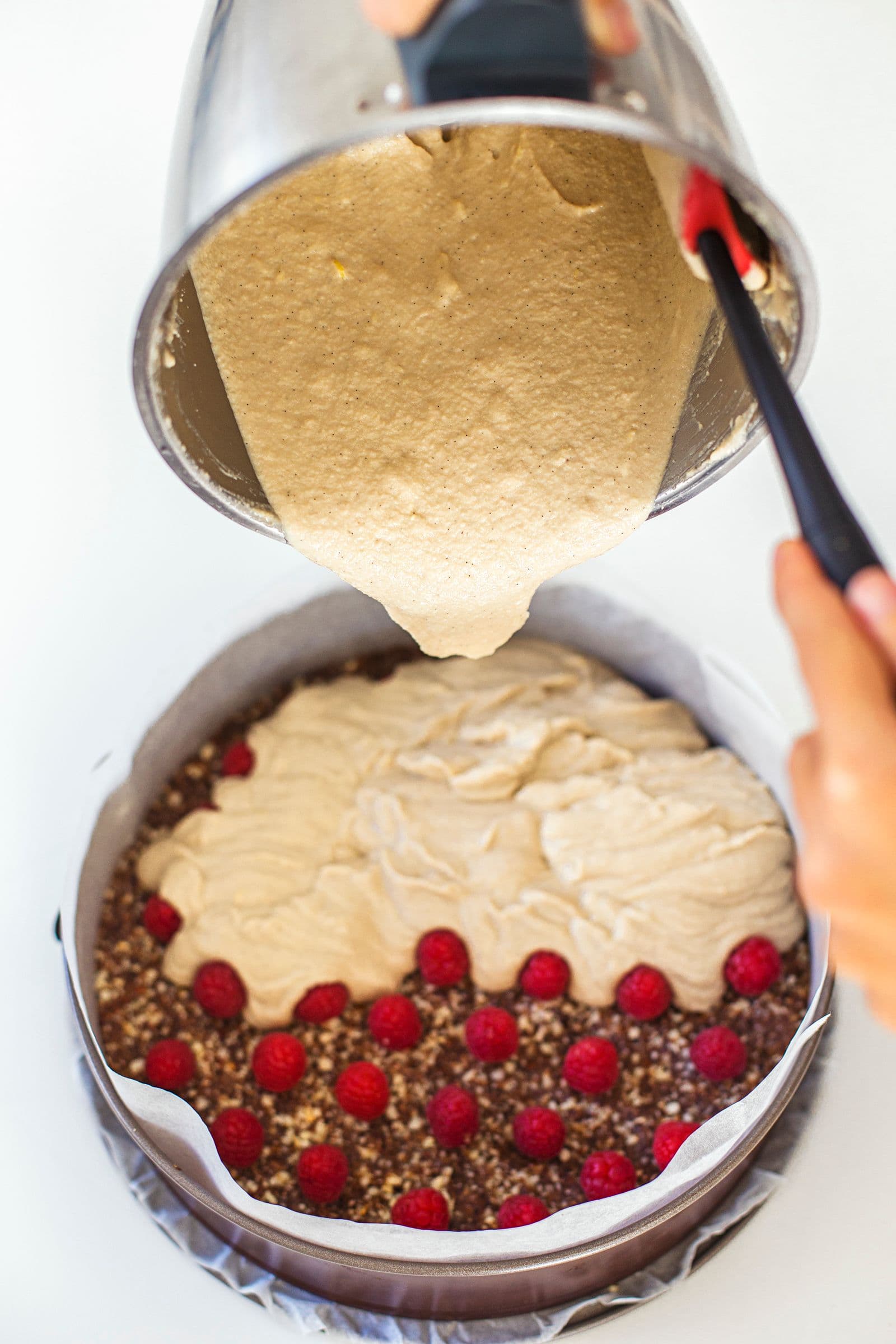 Recheio de cheesecake vegan a ser vertido sobre as framboesas na forma.