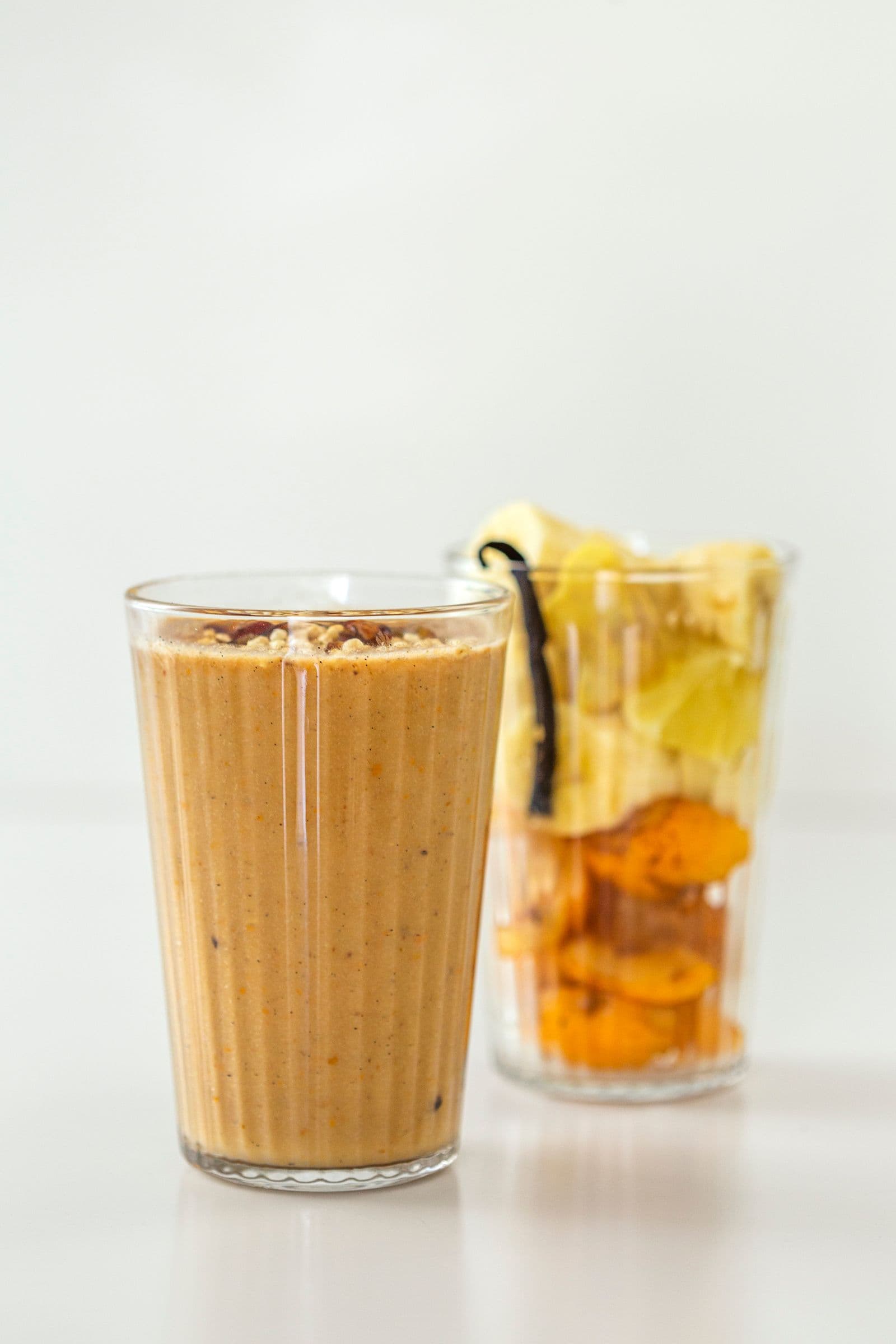 Loquat, ginger and vanilla smoothie in a glass, with a second glass of fresh ingredients slightly blurred in the background