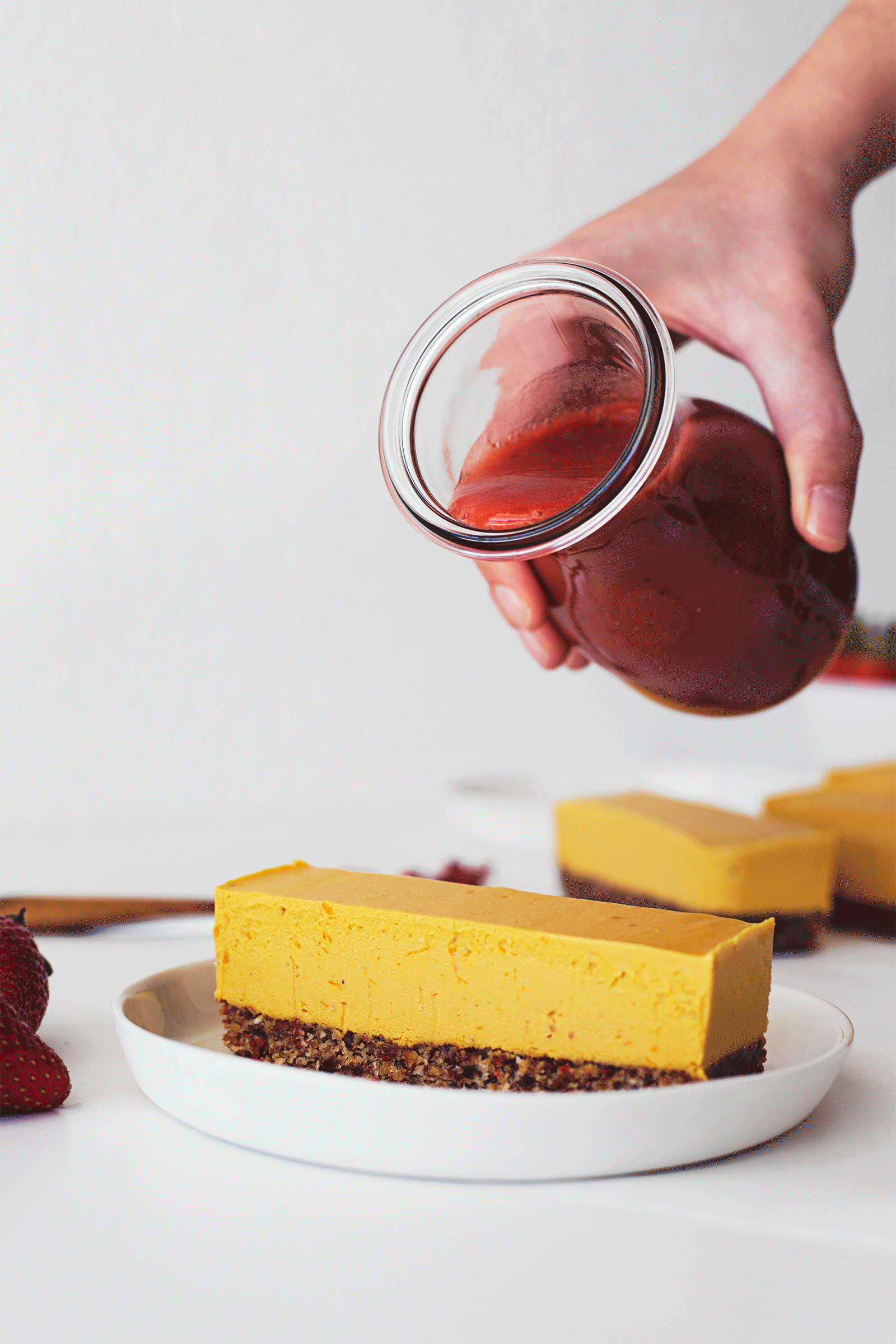 Gif animado de uma mão a verter molho de morango sobre o cheesecake vegan de laranja e goji.