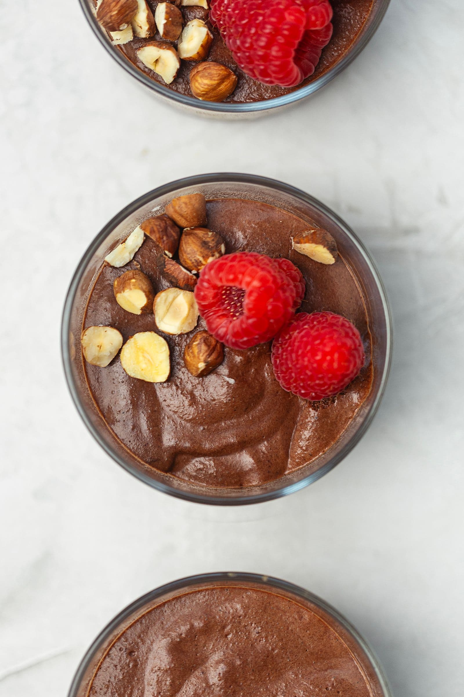 Mousse de chocolate vegan decorada com framboesas frescas e avelãs tostadas.