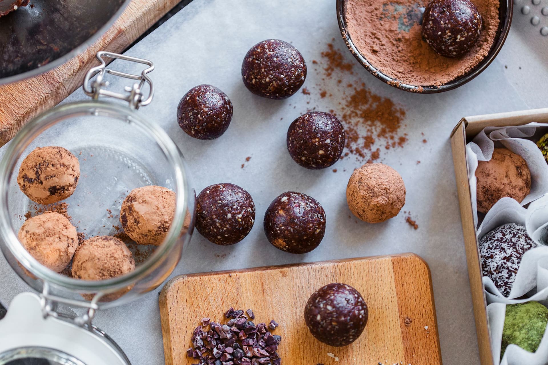 Glass jar and wooden board with cacao almond energy balls and cocoa powder.