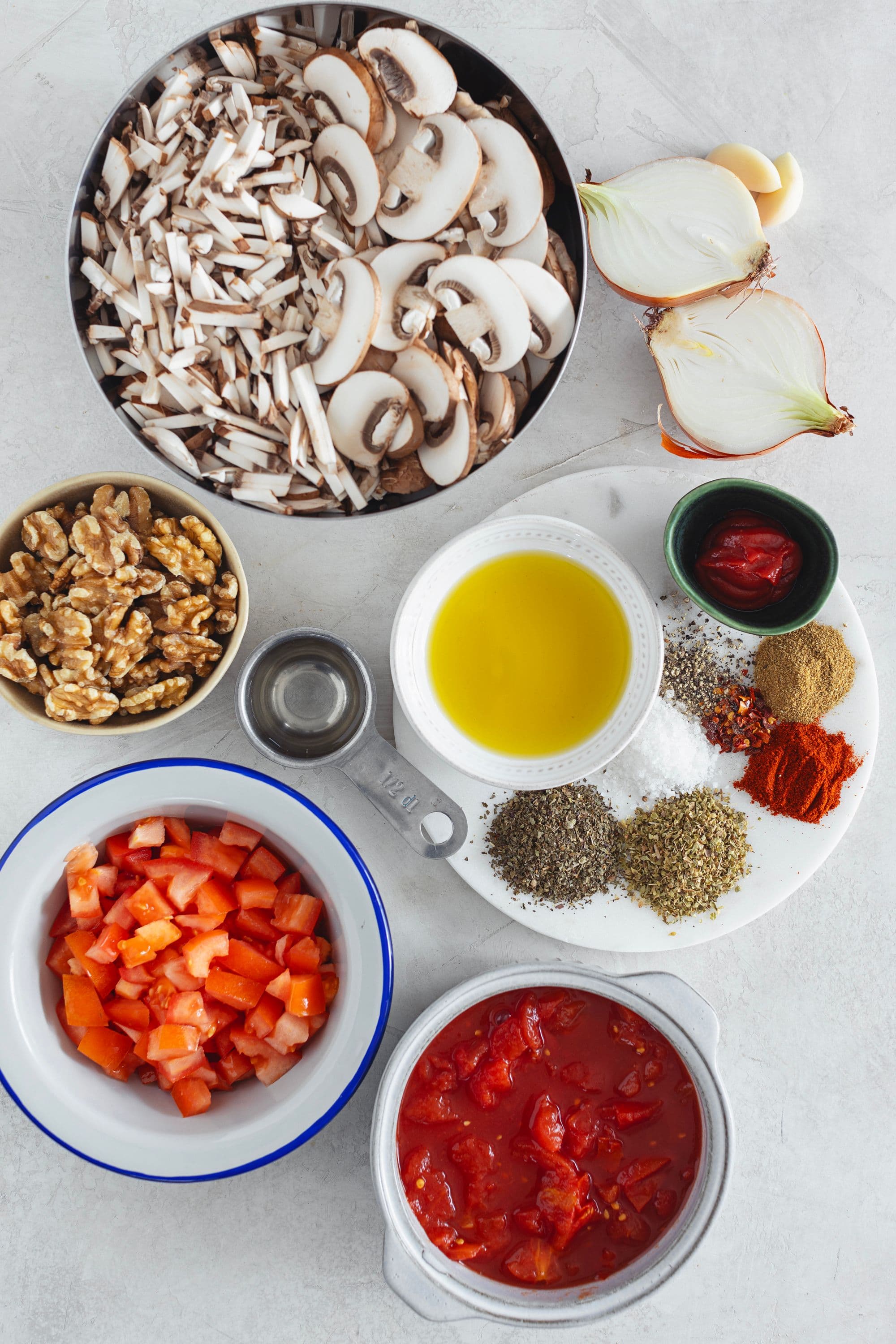 All ingredients laid out for vegan bolognese: mushrooms, walnuts, onion, tomato, herbs and oil.