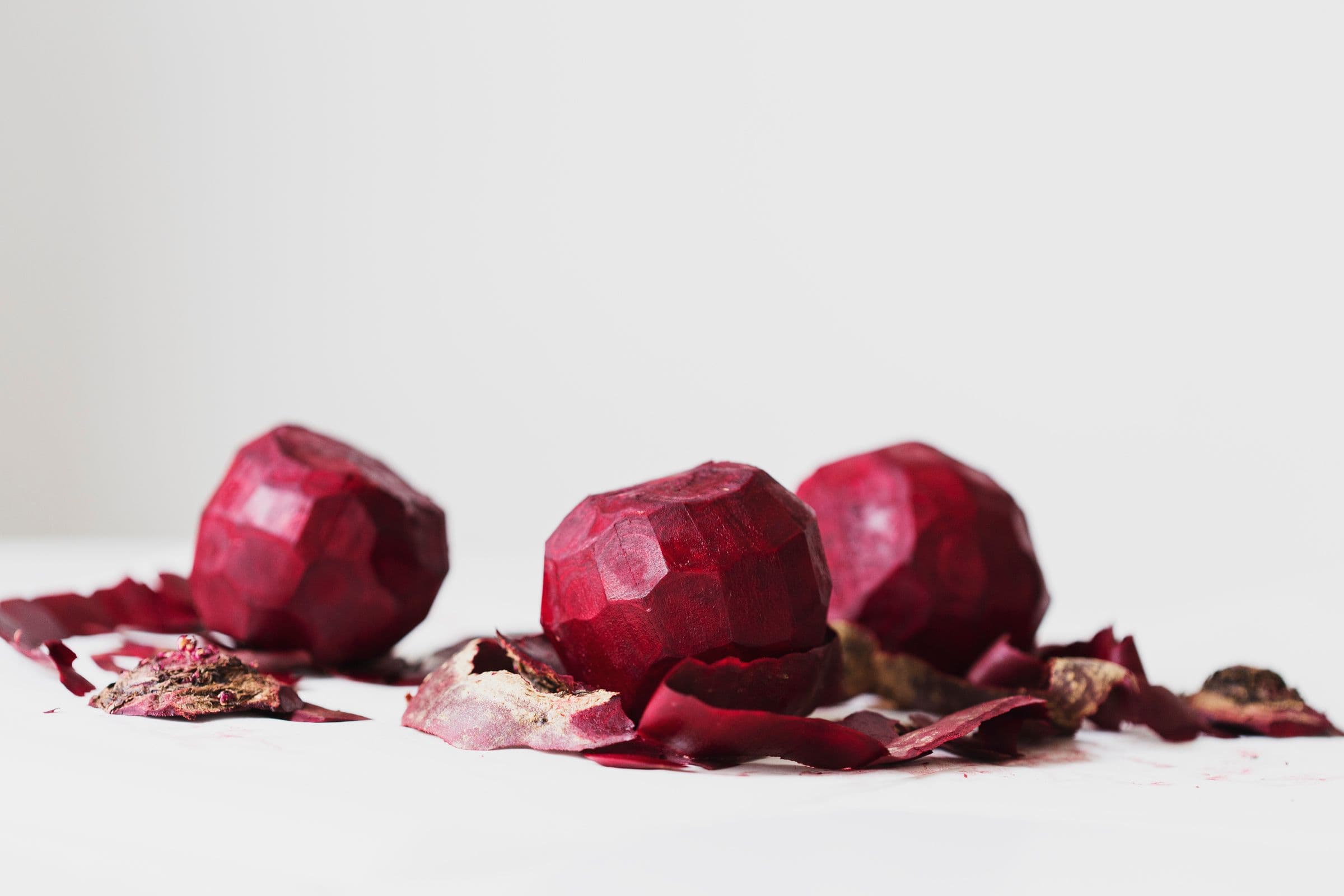 Whole raw beetroots with their peels, placed on a white surface.