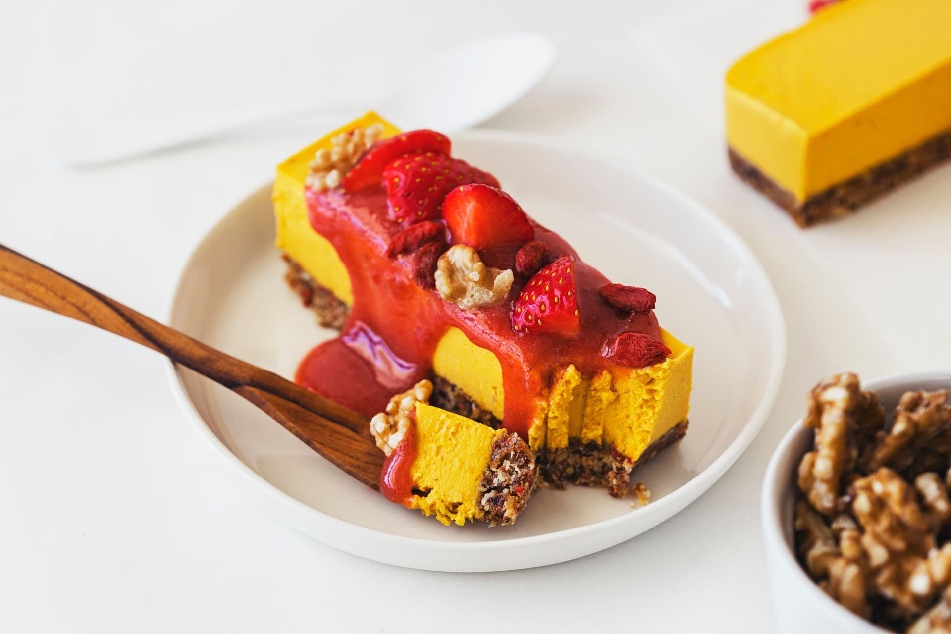 Beautifully decorated raw vegan cheesecake on a small, white dish with a wooden fork.