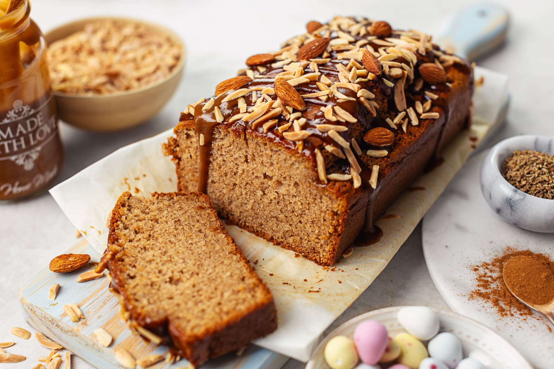 Vegan almond cake cut open with a slice in front revealing the soft interior, topped with caramel and almonds.