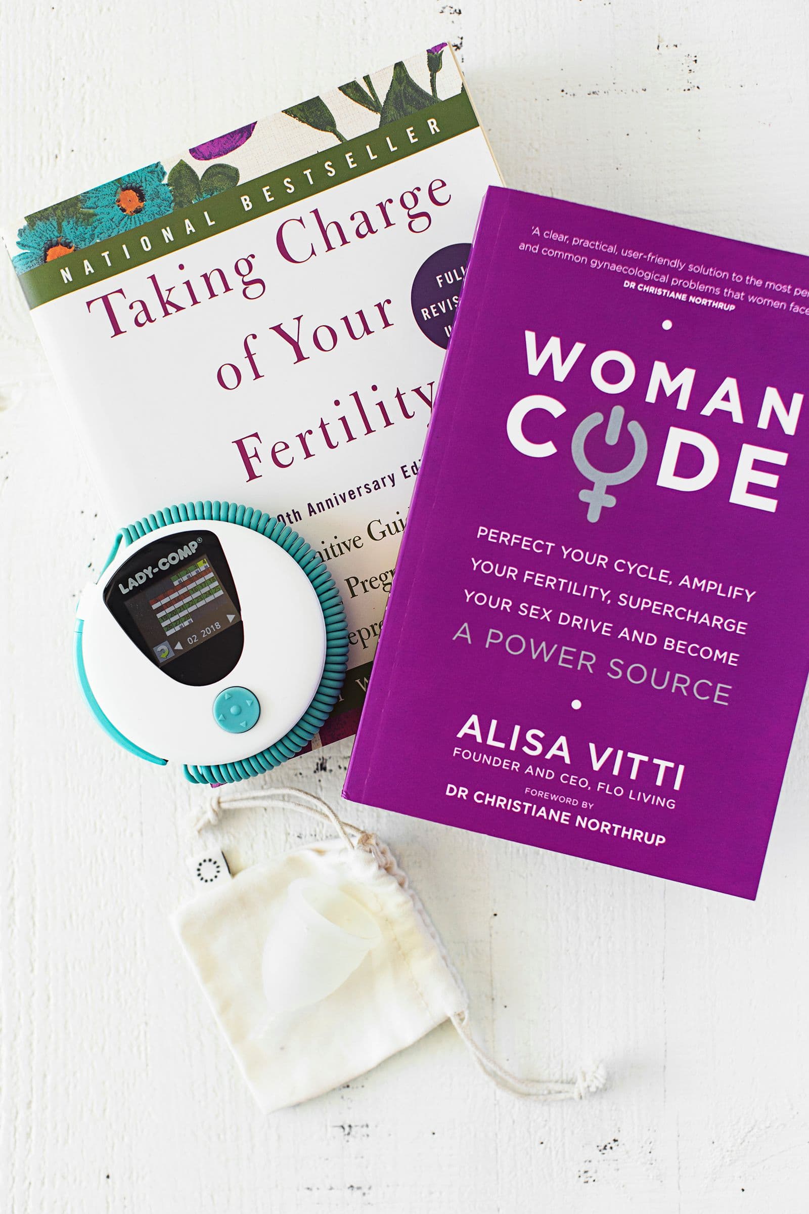 Termómetro de temperatura basal e livros sobre equilíbrio hormonal dispostos numa superfície branca.