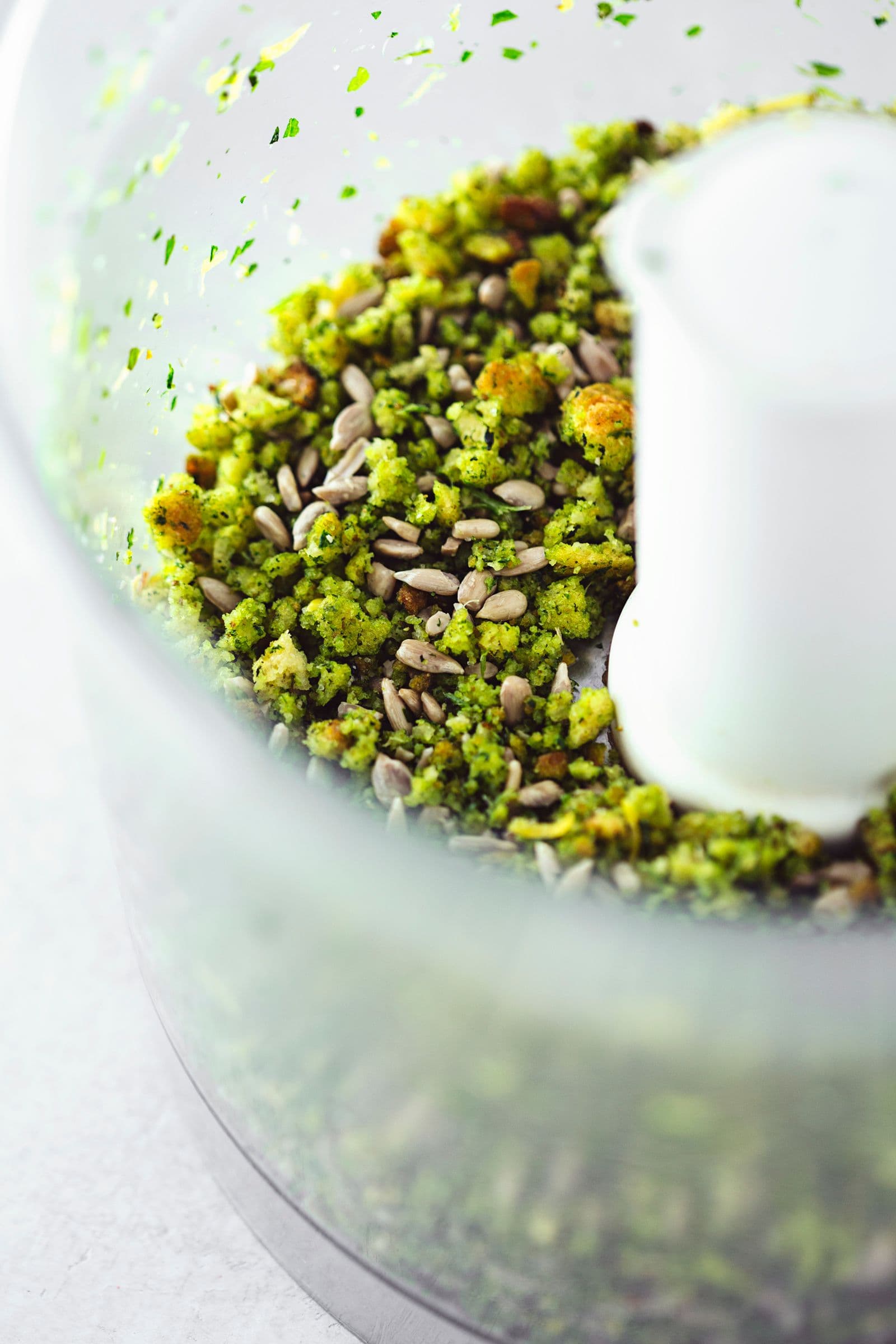 Cornbread crumble inside a food processor, already pulsed with fresh herbs, seasonings and sunflower seeds.