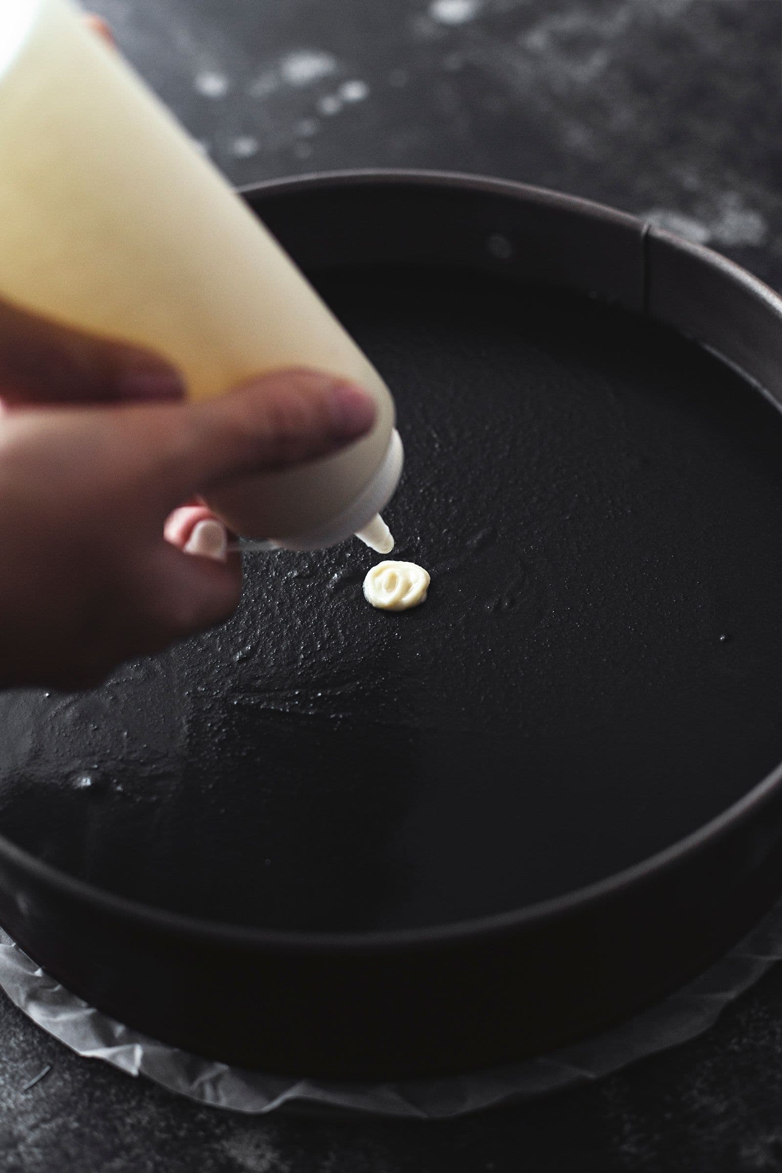 Hand piping white chocolate on top of a dark chocolate cheesecake to start a spiderweb pattern.