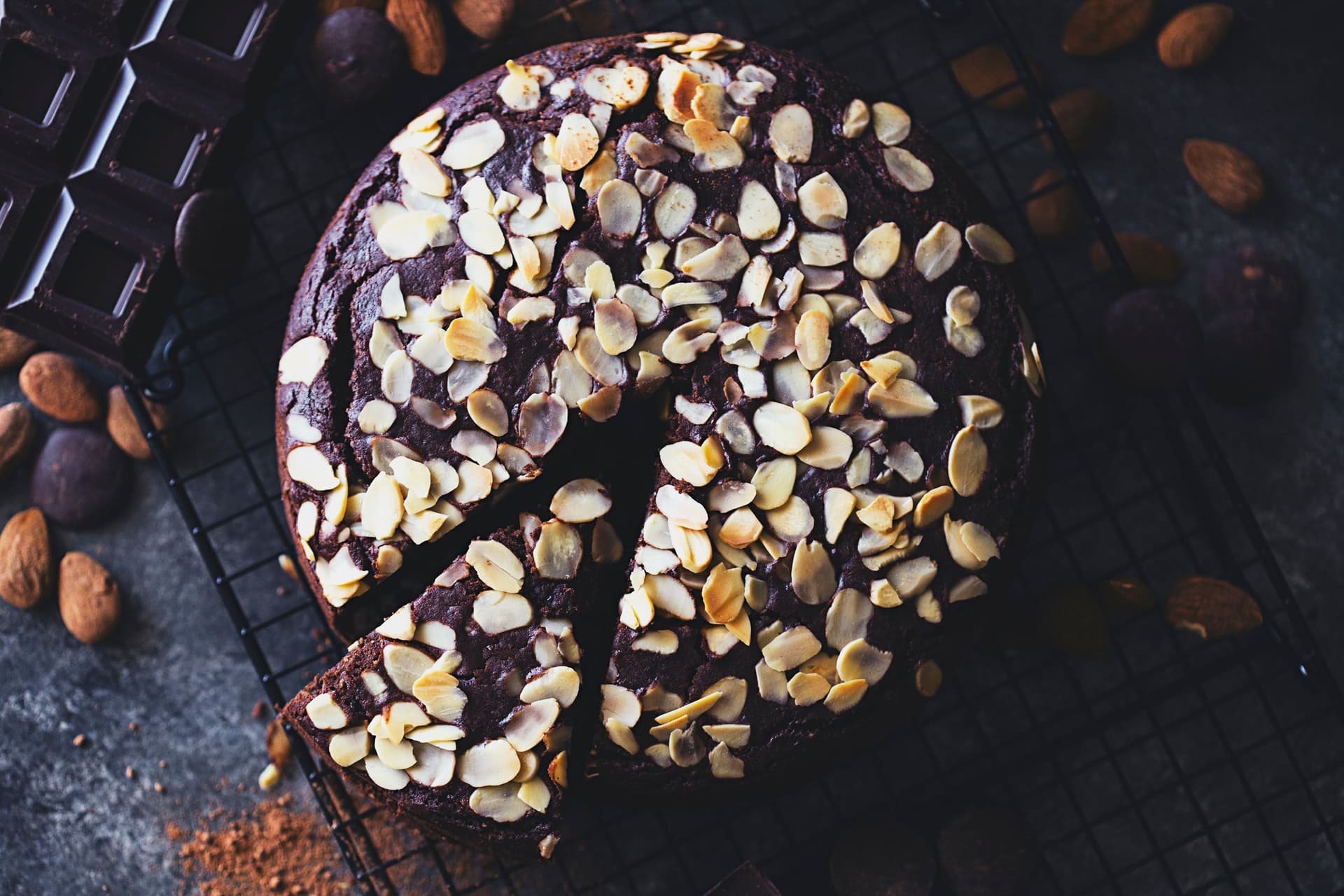Overhead view of a sliced chocolate cake topped with almond flakes, placed on a cooling rack.