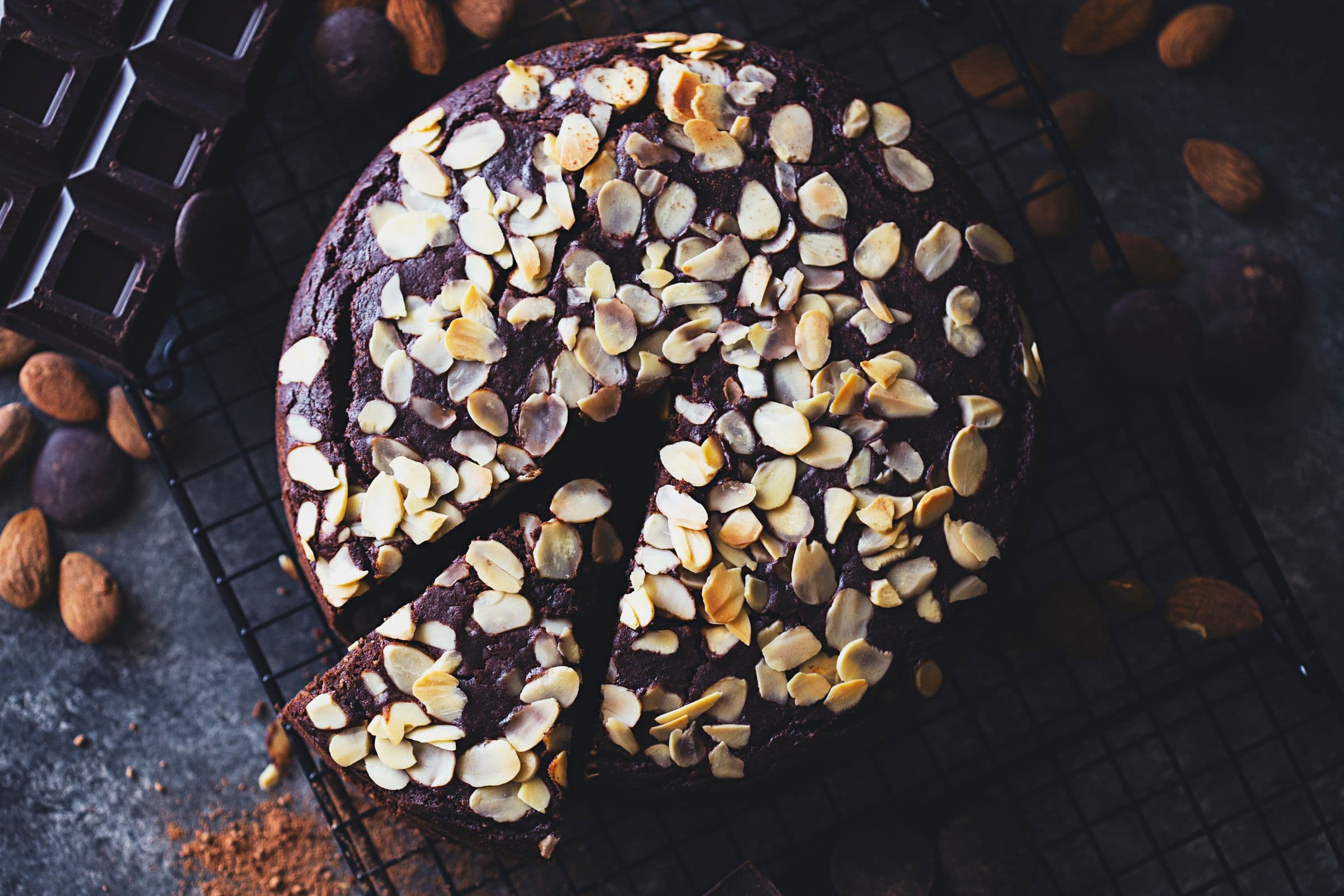 Overhead view of a sliced chocolate cake topped with almond flakes, placed on a cooling rack.