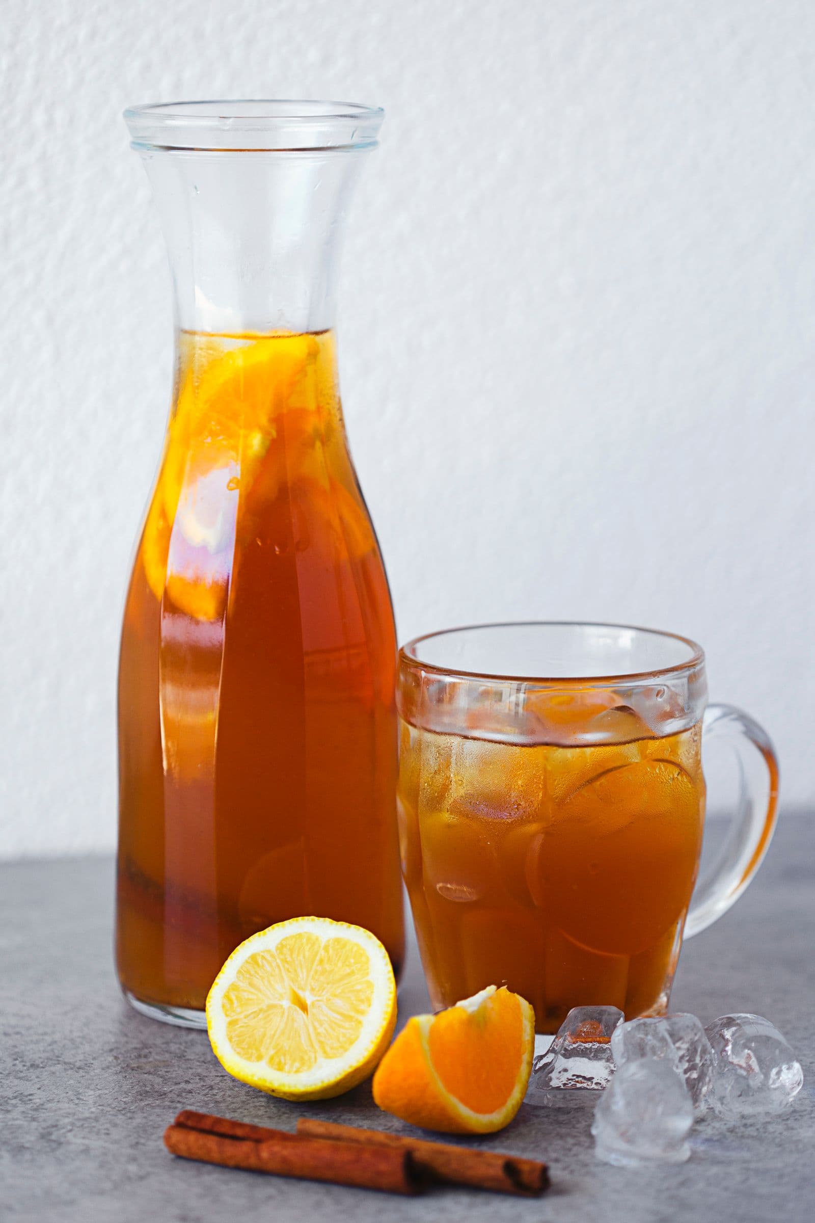 Carafe and glass filled with iced tea, garnished with lemon and orange slices, with ice cubes.