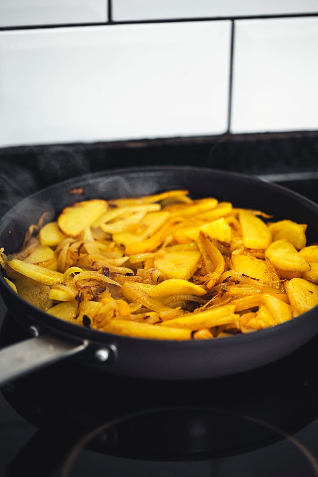 A black skillet with sautéed golden potato slices, cooked and softened.