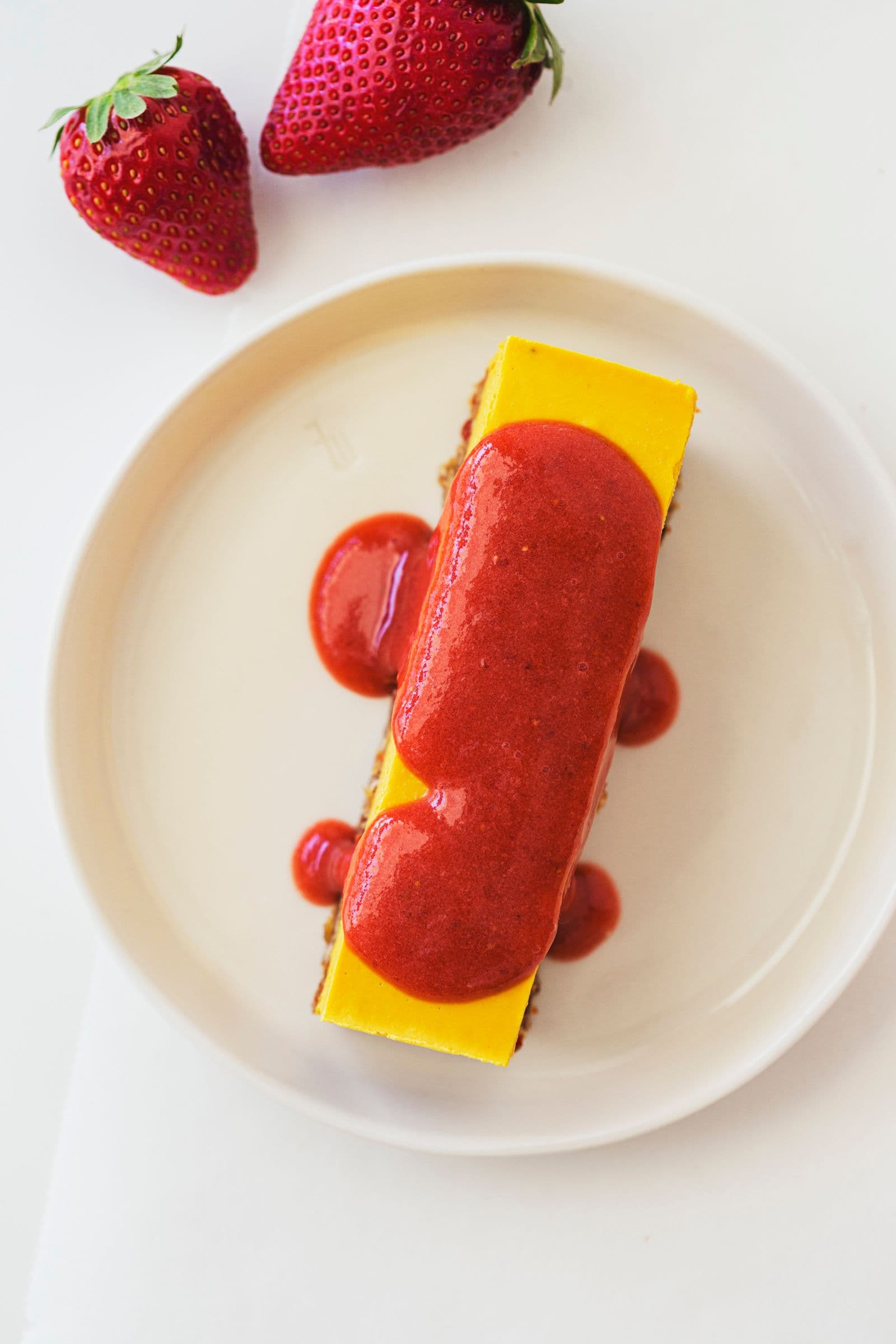 Single cheesecake slice served on a plate with strawberry sauce.