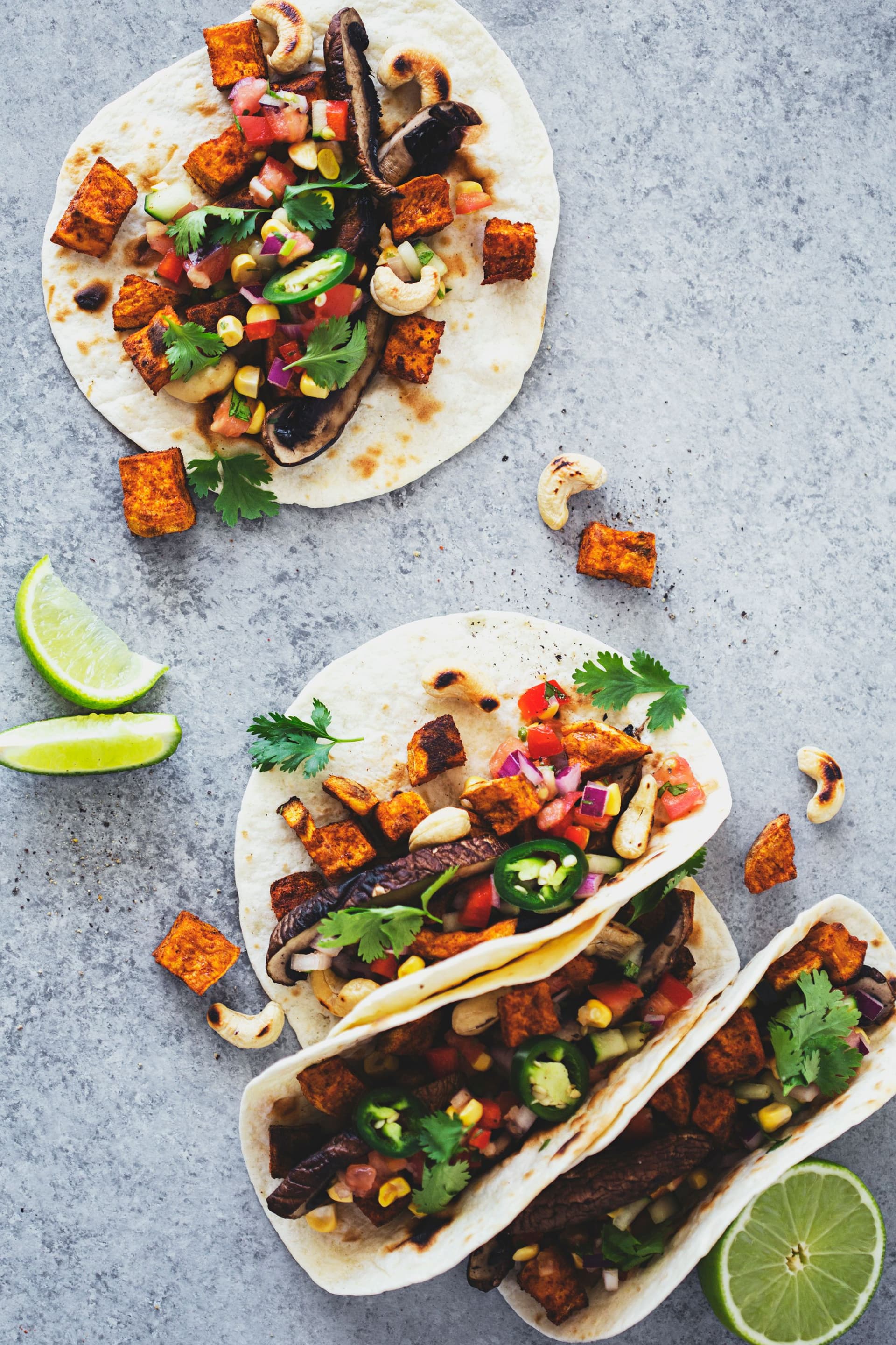 Vista de cima de tacos com vegetais grelhados e coberturas frescas, acompanhados de gomos de lima.