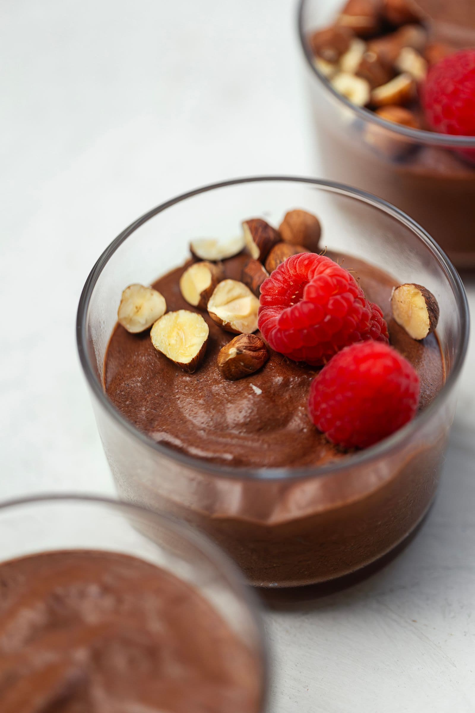 Close-up de mousse de chocolate vegan num copo de vidro, com framboesas e frutos secos.