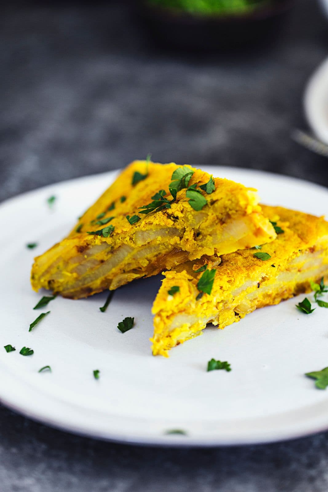 Fatias triangulares de tortilha espanhola vegan num prato branco, polvilhada com salsa.